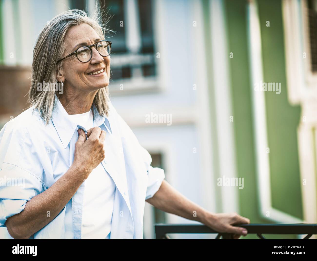 Glück im Alter, reife Frau mit strahlendem Lächeln auf dem Balkon mit Blick auf die alte Straße in Europa. Senior Lady in Joyfu Stockfoto