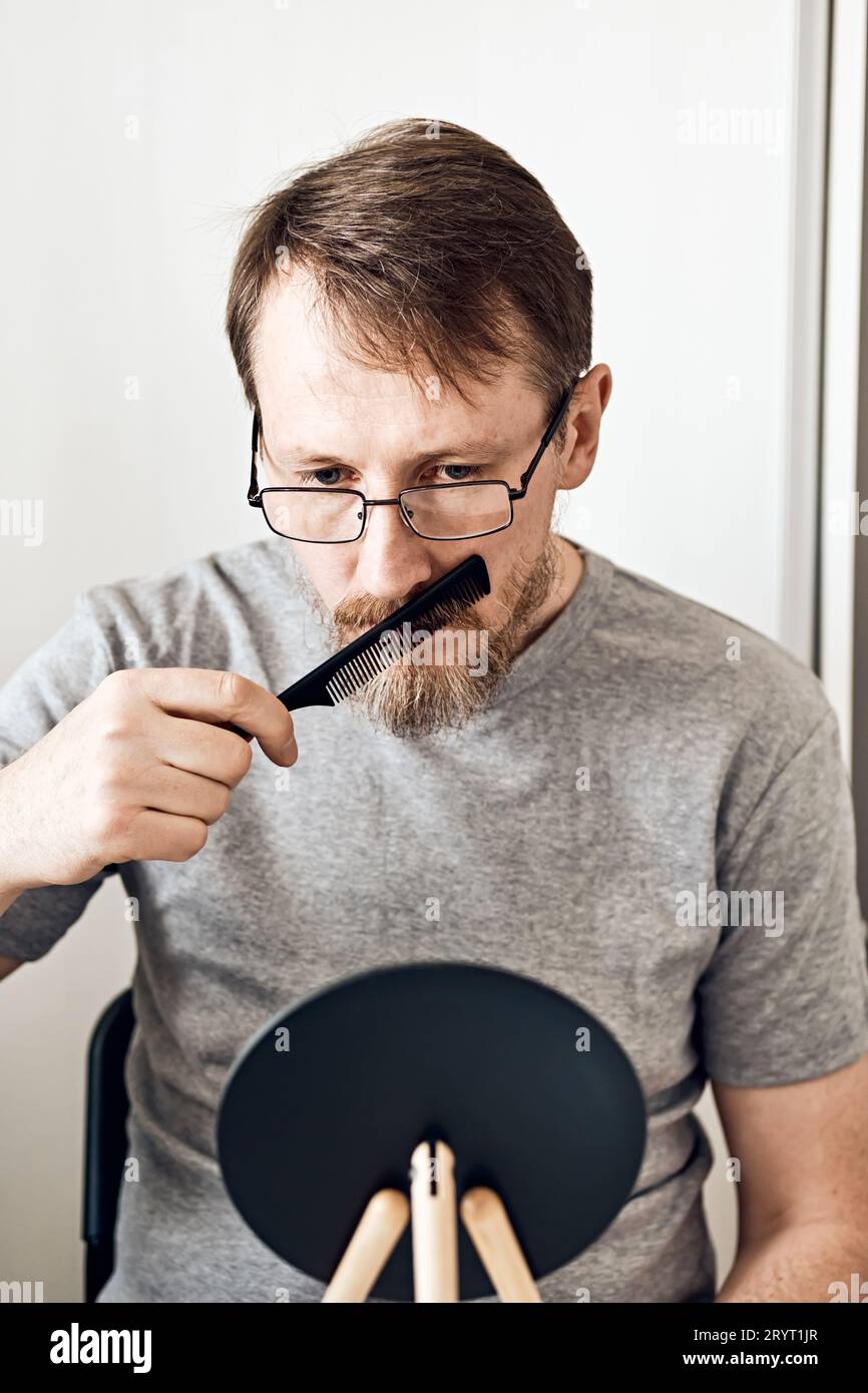 Ein attraktiver Mann mittleren Alters streckt seinen Bart vor einem Spiegel. Natürlicher Look, hellblondes Haar und Sommersprossen, Bartverstand Stockfoto