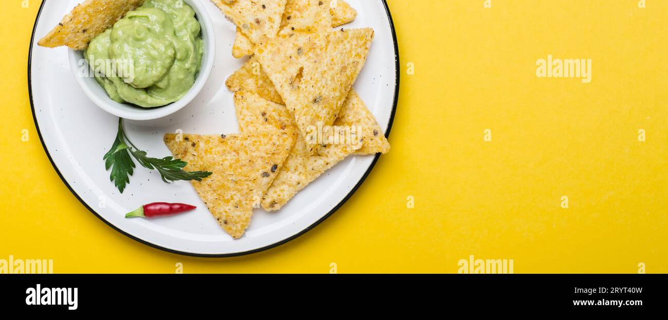 Traditionelle lateinamerikanische Guacamole mit Corn Chips Nachos auf gelbem Hintergrund. Bannerformat Stockfoto
