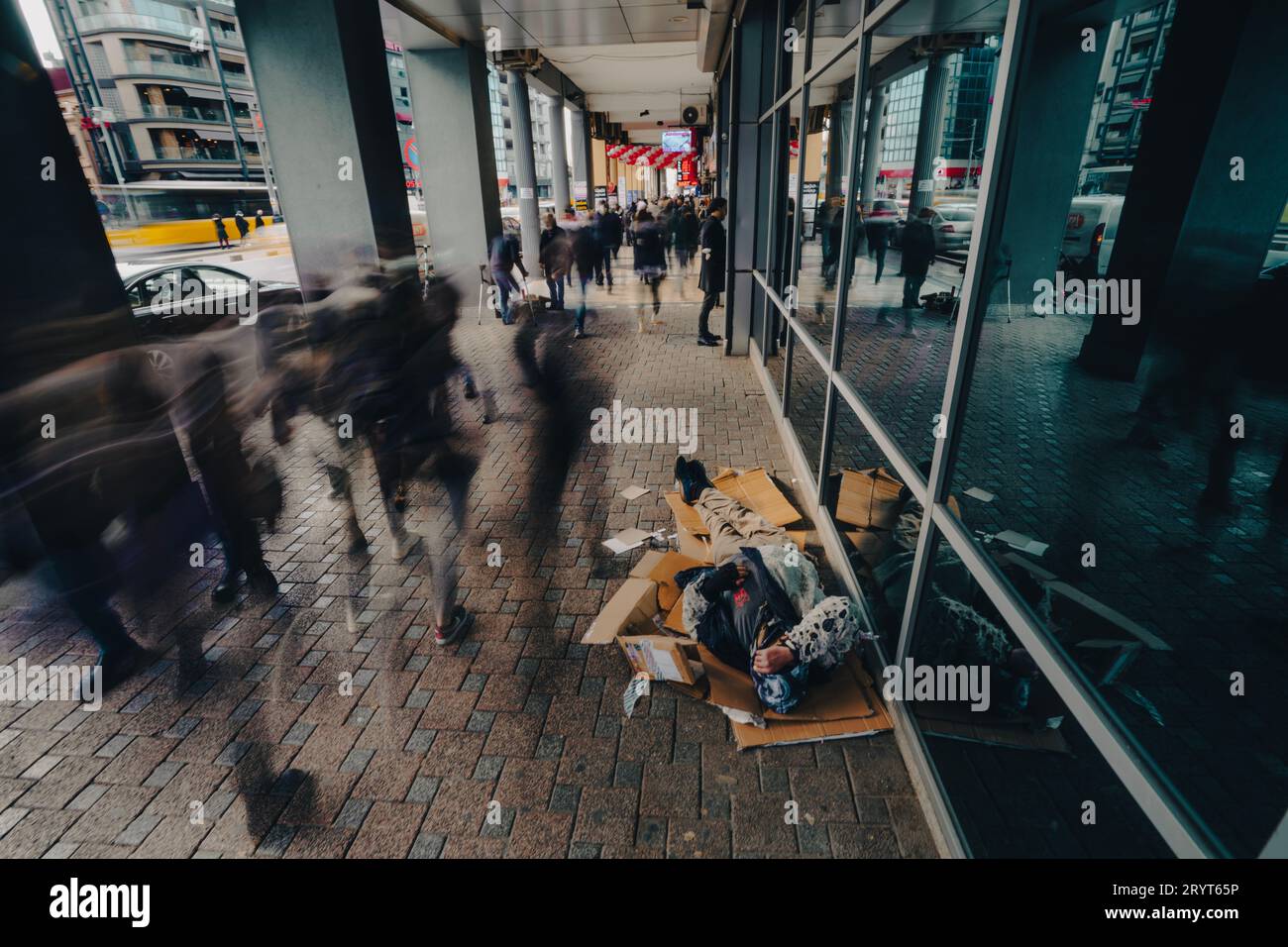 Eine obdachlose Person, die draußen auf dem Boden liegt und in einem Notstand ist, mit vorbeiziehenden Menschen Stockfoto