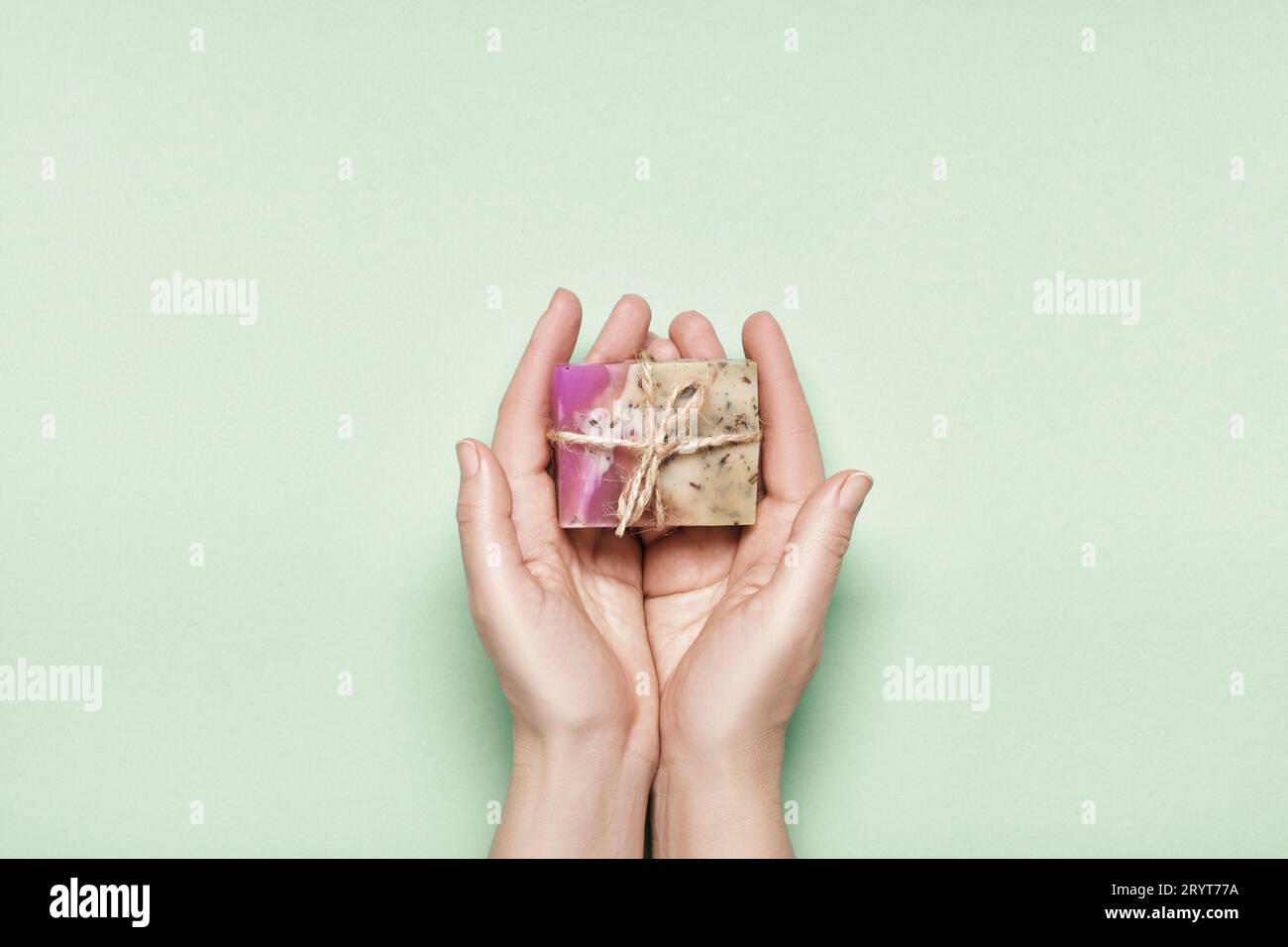 Selbstgemachte Seife aus Kräuterabkochen in weiblichen Händen auf grünem Hintergrund. Naturkosmetik-Geschenk Stockfoto