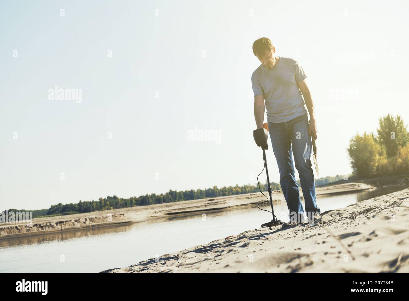 Mann mit Metalldetektor läuft am Sandufer entlang. Suche nach Schätzen und Metall zum Recycling Stockfoto