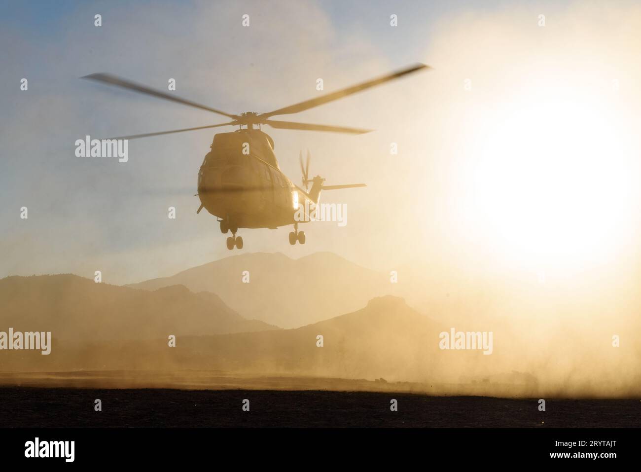 Ein Militärhubschrauber fliegt und landet in der Wüste bei Sonnenuntergang in einer Staubwolke. Luftwaffe Stockfoto