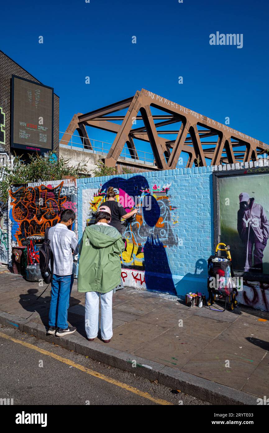 Brick Lane Graffiti. Touristen beobachten, wie ein Graffiti-Künstler in Brick Lane East London ein Werk kreiert. Stockfoto