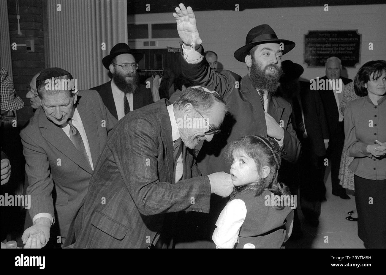 Die Upshernish erste Haarschneidezeremonie für einen dreijährigen jüdischen Jungen. Es ist eine altehrwürdige jüdische Tradition, einem Jungen das Haar in den ersten Lebensjahren unberührt wachsen zu lassen.1 an seinem dritten jüdischen Geburtstag werden Freunde und Gemeindemitglieder zu einer festlichen Haarschneidezeremonie eingeladen: Das Hochgefühl („Scheren“) auf Jiddisch oder Chalakah auf Hebräisch. Hier ist Yehudah lieb Sohn des Rabbiners Herchel Rader von der Solihull-Gemeinde das glückliche Thema. Die Mitglieder der Gemeinde sind an der Reihe, um dem jungen Mann ein kleines Stück Haar zu schneiden. Stockfoto