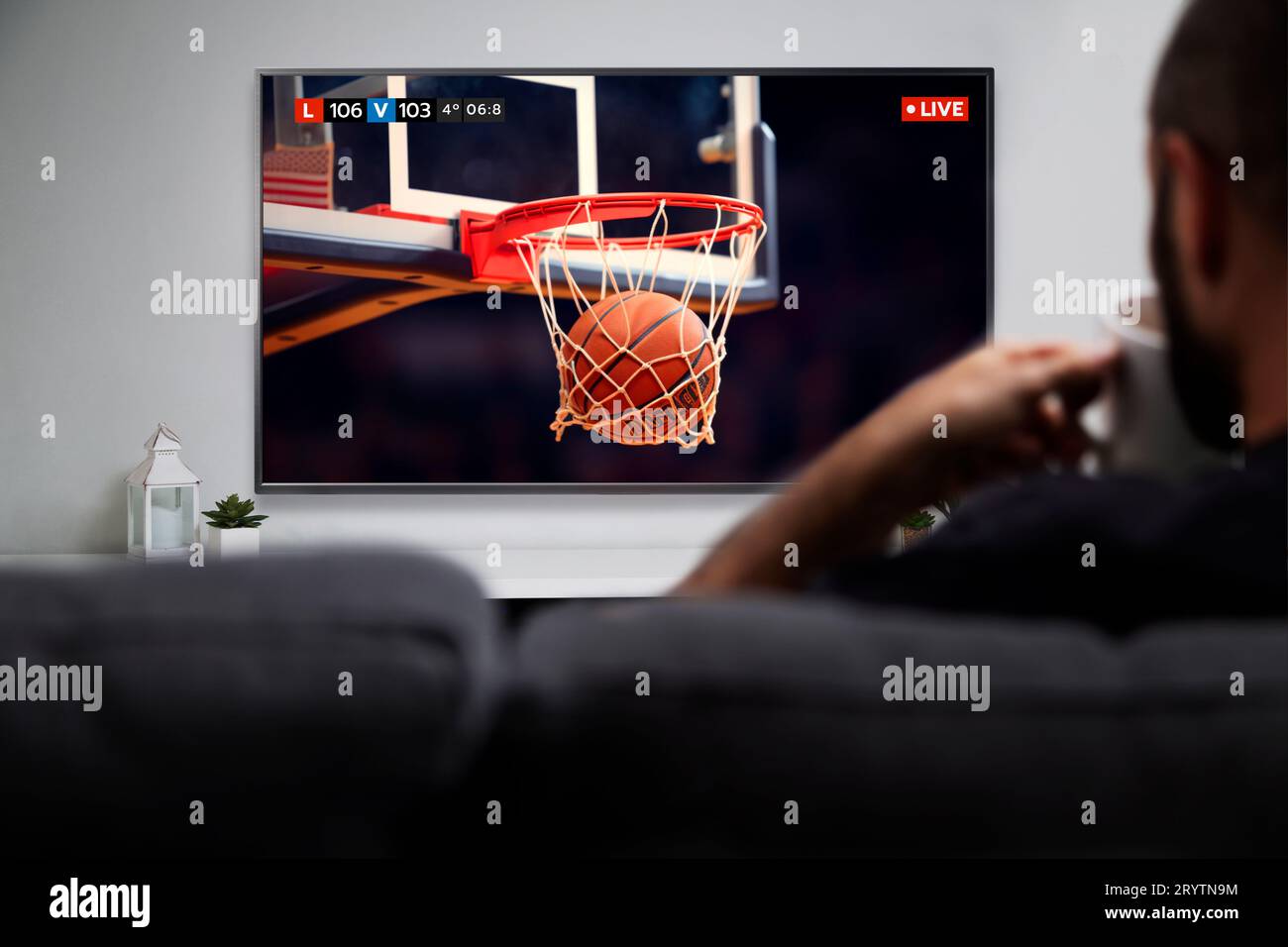 Mann, der Basketballspiele im Smart-TV ansieht, während er Kaffee trinkt. Abbildung: Kugel, die in den Ring eindringt. Live-TV-Übertragung. Stockfoto