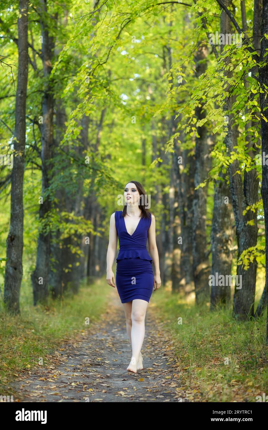 Frau in blauem Kleid, die entlang der Herbstlindenallee läuft. Stockfoto