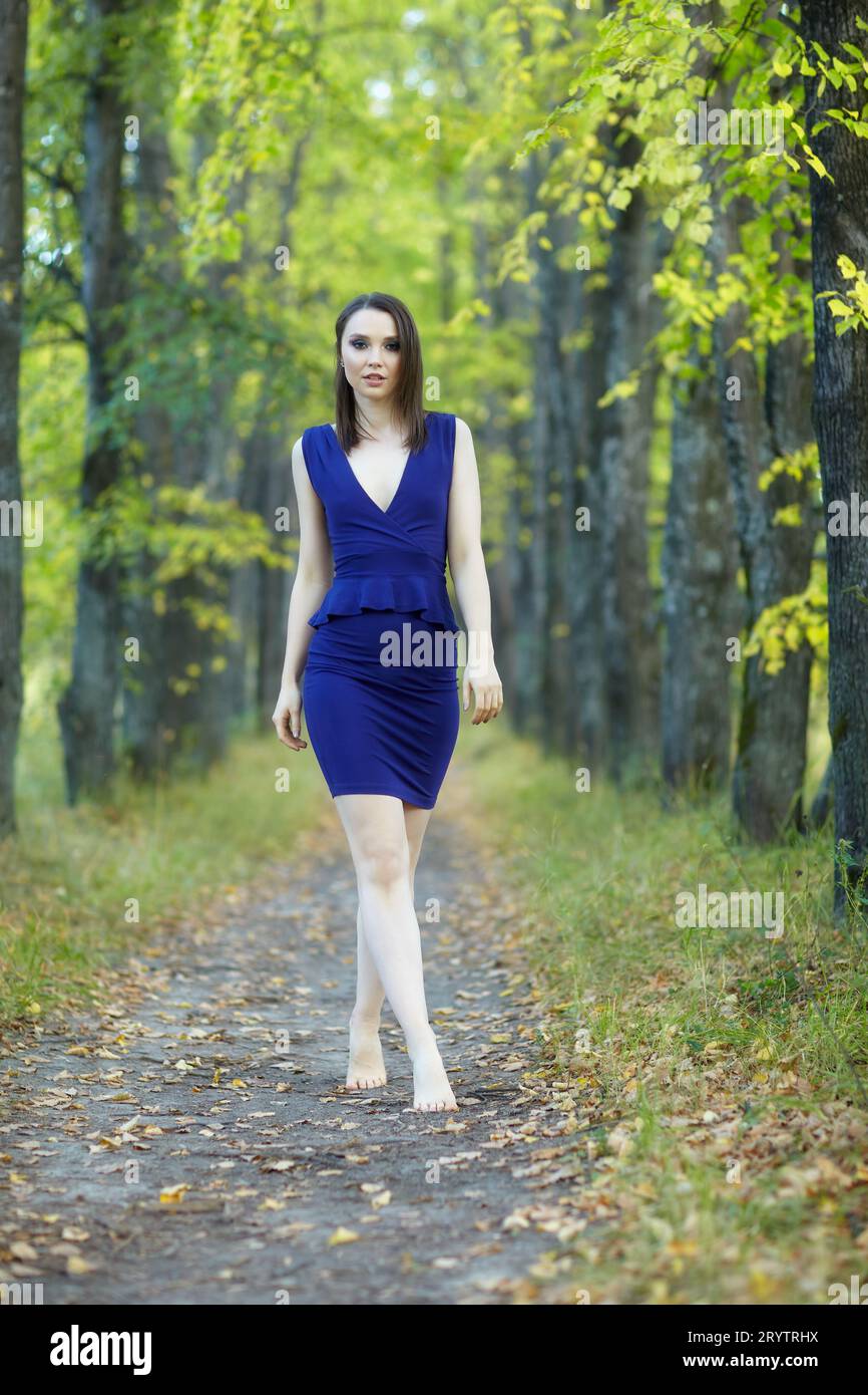 Frau in blauem Kleid, die entlang der Herbstlindenallee läuft. Stockfoto