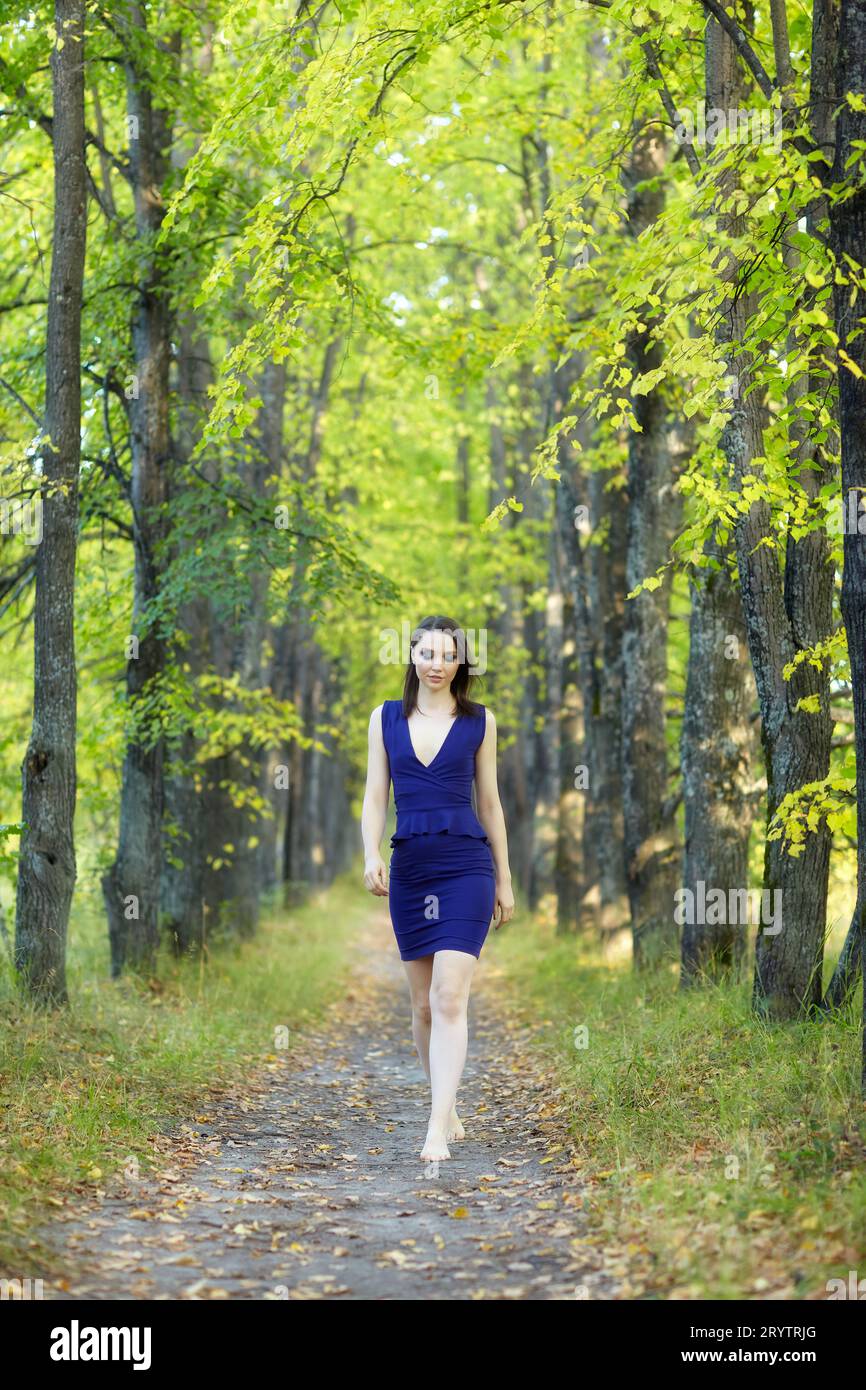 Frau in blauem Kleid, die entlang der Herbstlindenallee läuft. Stockfoto