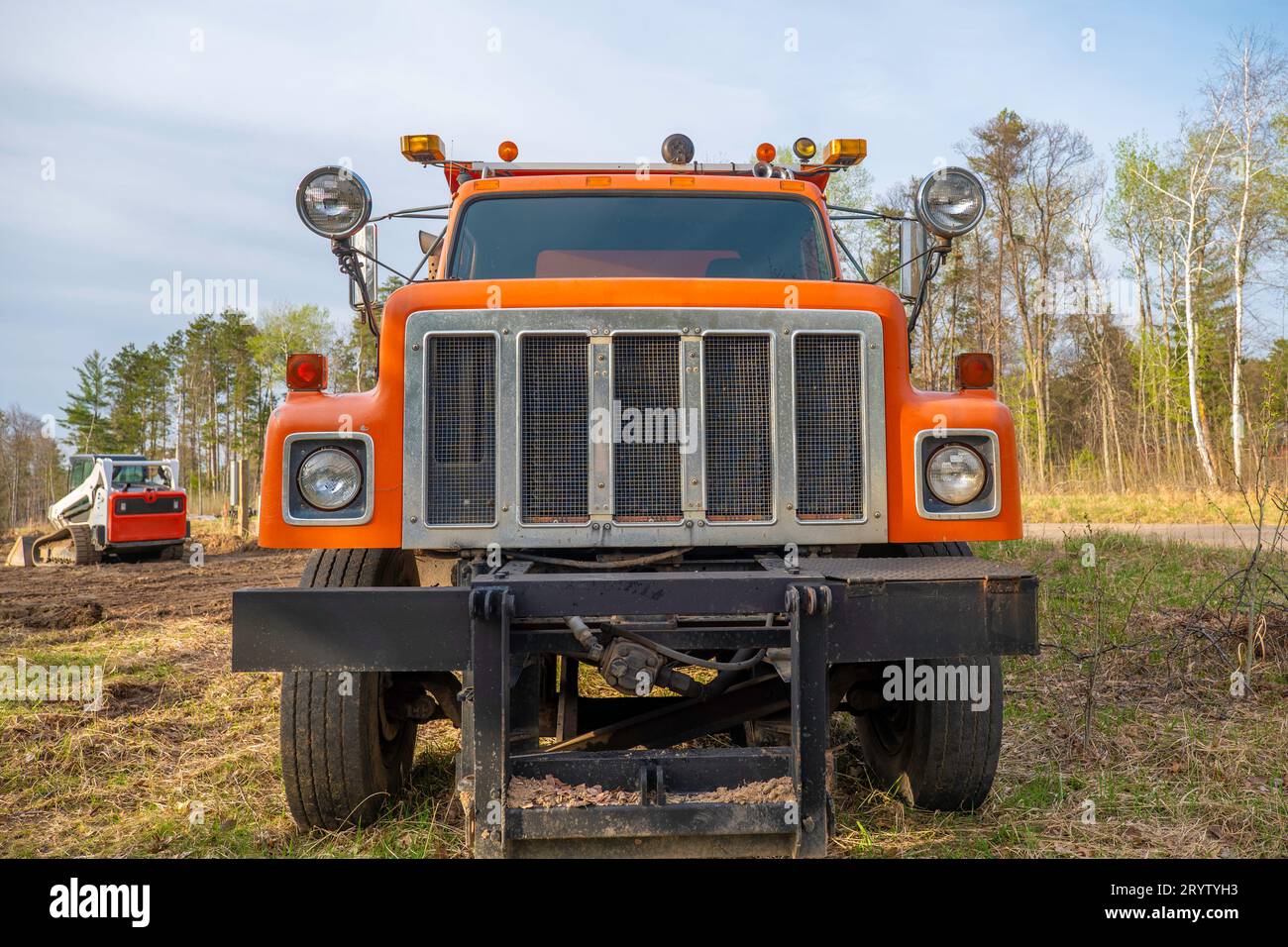 Nahaufnahme der linken Vorderseite eines älteren, gut gebrauchten orangen Muldenkippers auf einer Baustelle. Stockfoto