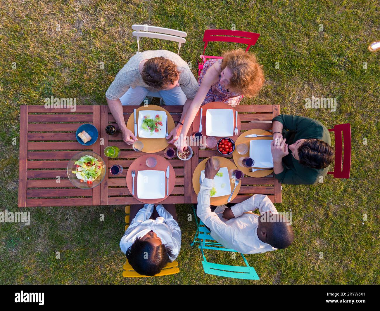 Multi ethnische Gruppe junger Freunde, die gemeinsam im Freien auf einer Sommergartenparty essen. Aus der Vogelperspektive auf den Tisch mit Speisen und Getränken Stockfoto