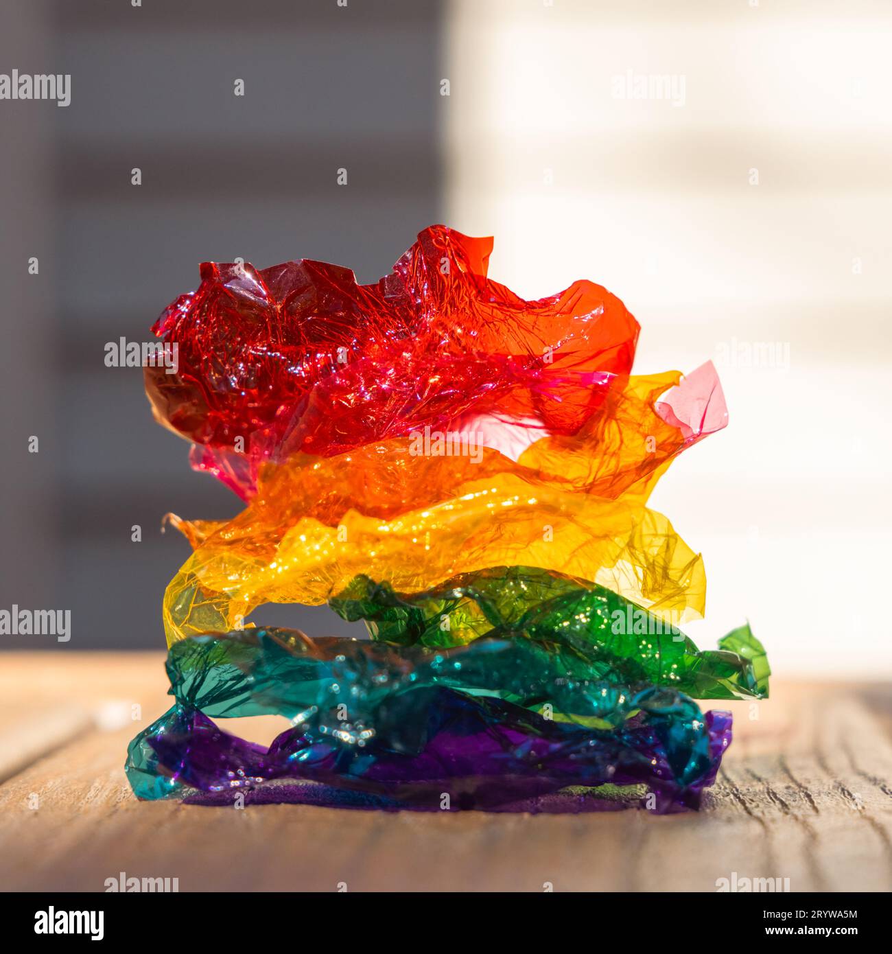 Regenbogenhaufen aus farbigen süßen Plastikverpackungen – rot, orange, gelb, grün, türkisblau, violett – auf Holzoberfläche, vor einem glatten Hintergrund. Stockfoto