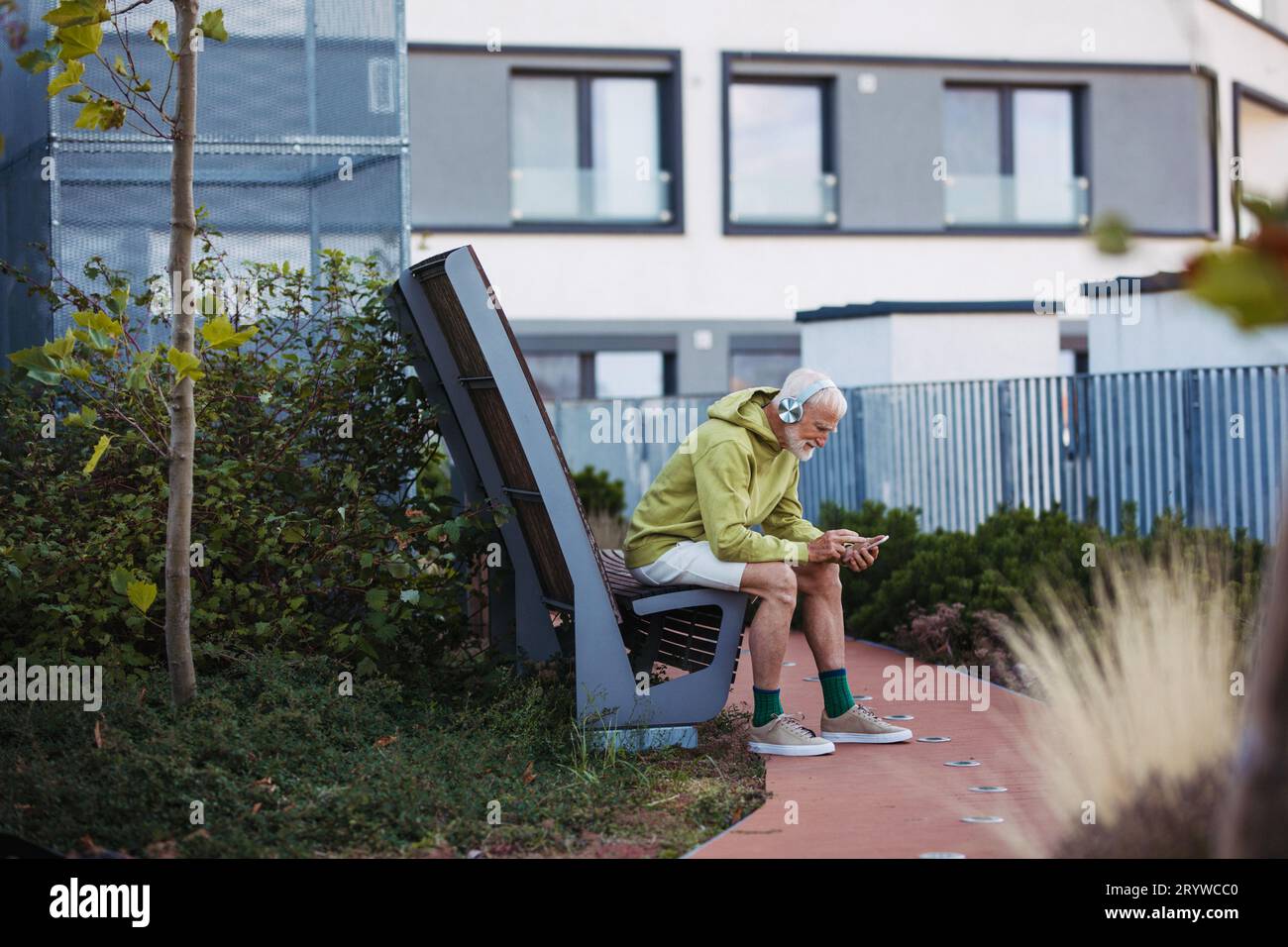 Älterer Mann, der Musik über kabellose Kopfhörer hört und sich auf seinen Morgenlauf vorbereitet. Stockfoto