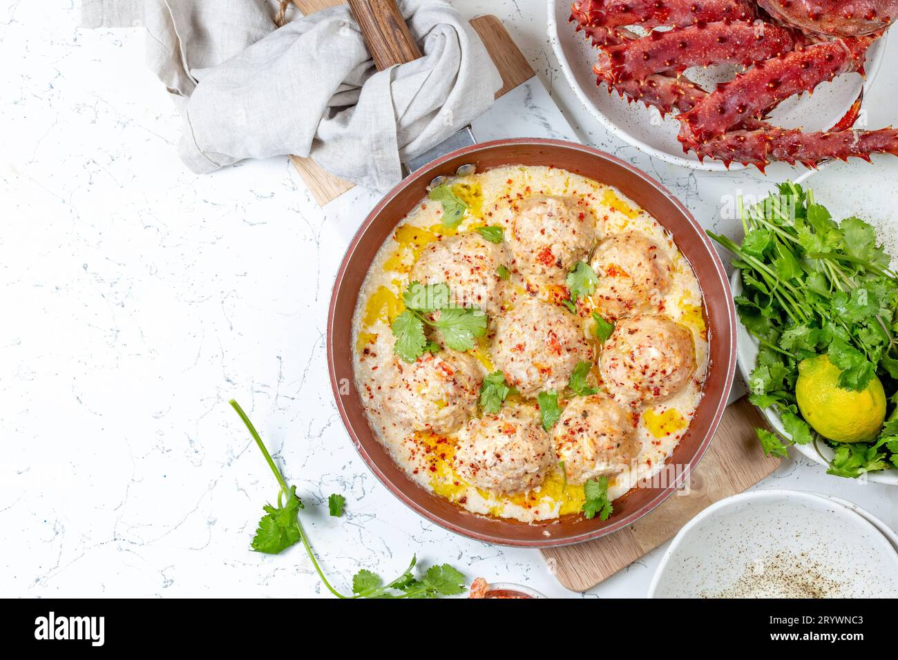 Krabbenfleischbällchen in weißer cremiger Sauce in Rotpfanne, ganze Königskrabbe, Koriander, Zitrone und Weißwein auf weißem Backgrou Stockfoto