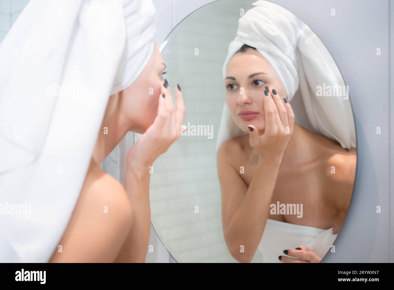Junge schöne Frau, die vor dem Spiegel Creme auf ihr Gesicht aufträgt Stockfoto