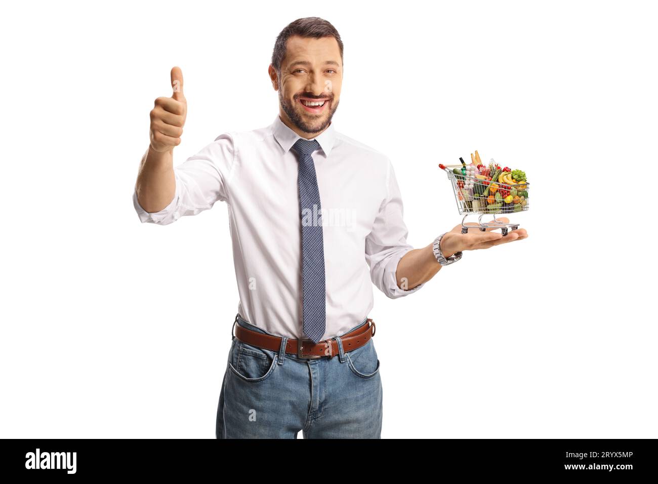 Junger, lächelnder Mann, der einen kleinen Einkaufswagen mit Essen hält und Daumen hoch bewegt, isoliert auf weißem Hintergrund Stockfoto