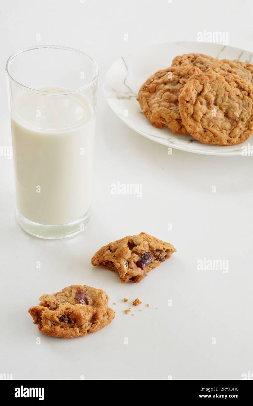 Haferflocken, Rosinen- und Walnusskekse mit hohem Glas Milch auf weißem Hintergrund im vertikalen Format. Selektive Fokussierung auf das vordere Stück des Kekses. Stockfoto