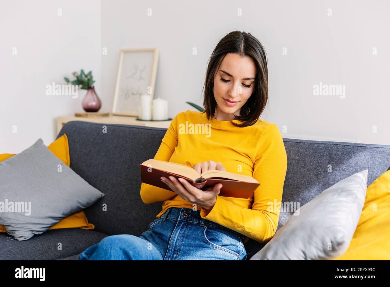 Eine entspannte junge Erwachsene Frau, die ein Buch liest und zu Hause auf der Couch sitzt Stockfoto
