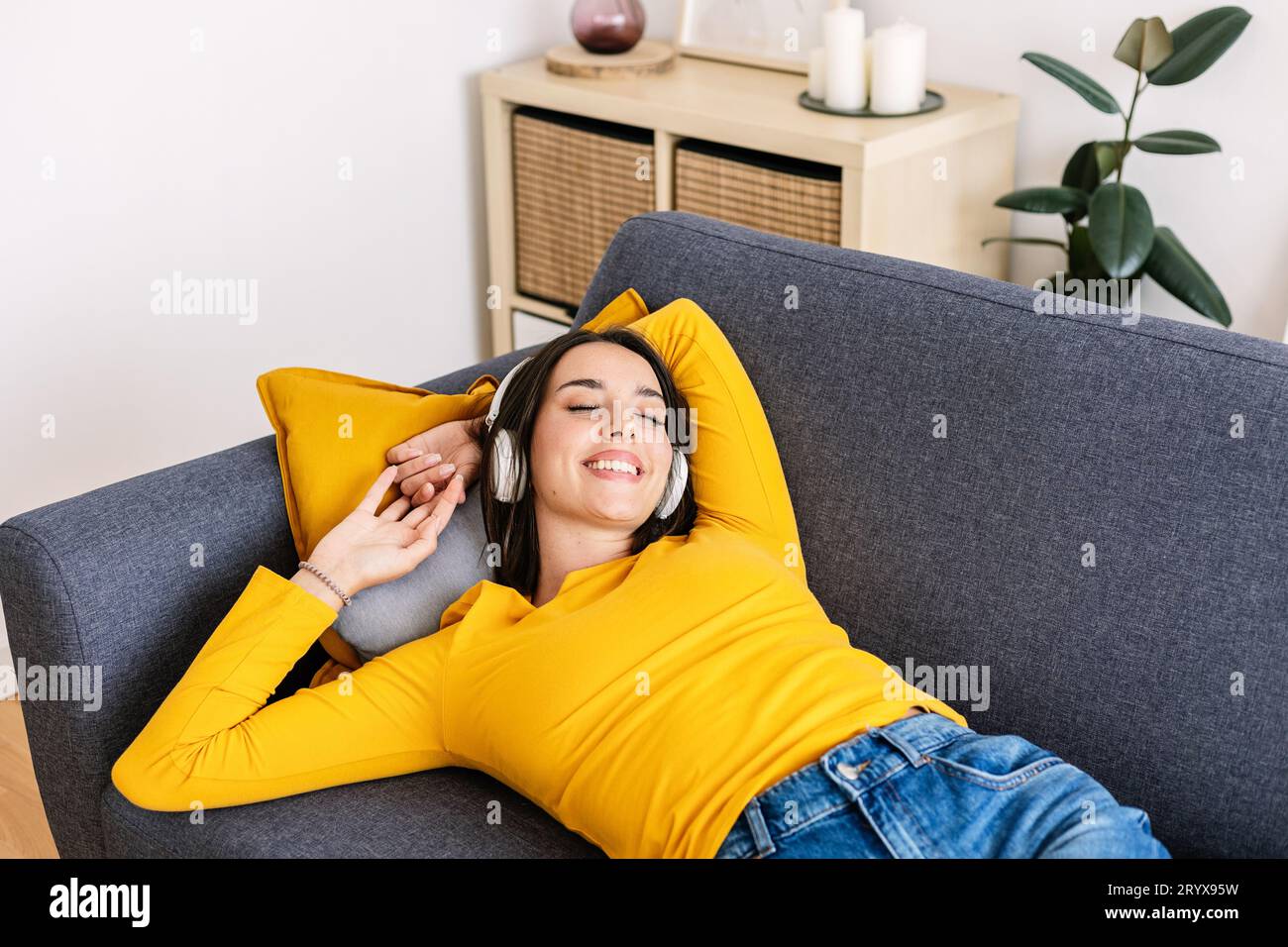 Junge glückliche Frau, die auf dem Sofa liegt und Musik mit Kopfhörern hört Stockfoto
