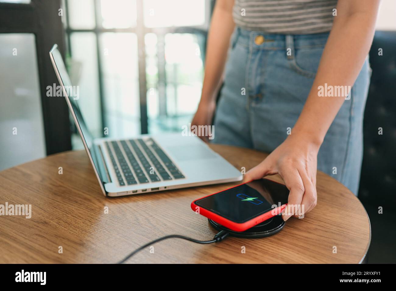 Laden des Mobiltelefonakkus mit drahtlosem Ladegerät im Tisch. Smartphone wird auf einem Ladepad aufgeladen. Mobiltelefon ne Stockfoto