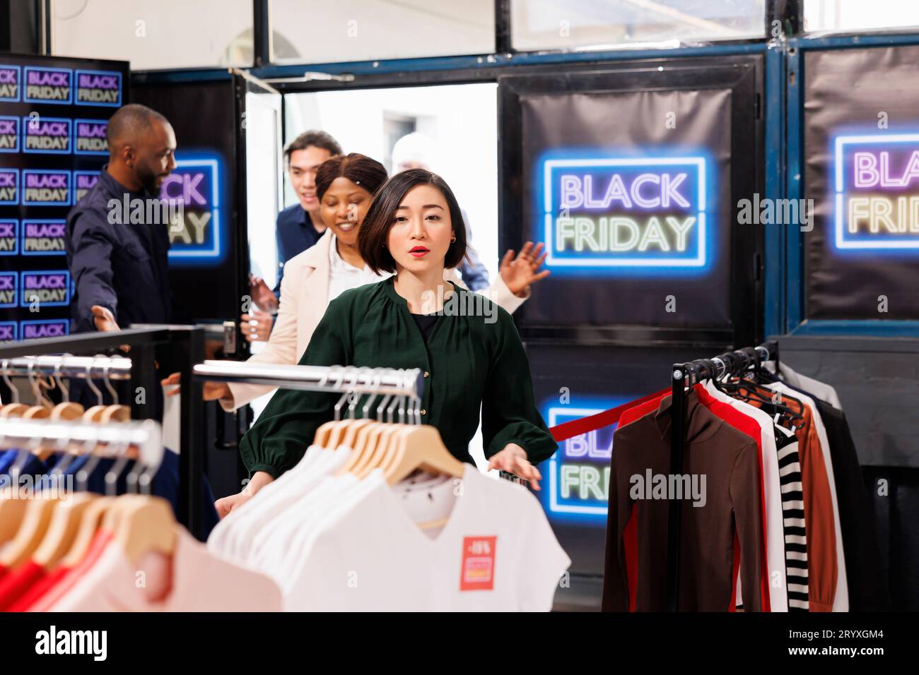 Ein lächelnder, freundlicher afroamerikanischer Sicherheitsbeamter öffnet die Tür des Bekleidungsgeschäfts und lädt am Black Friday Kunden am Eingang des Einkaufszentrums ein. Impulskäufe während der Verkaufssaison Stockfoto