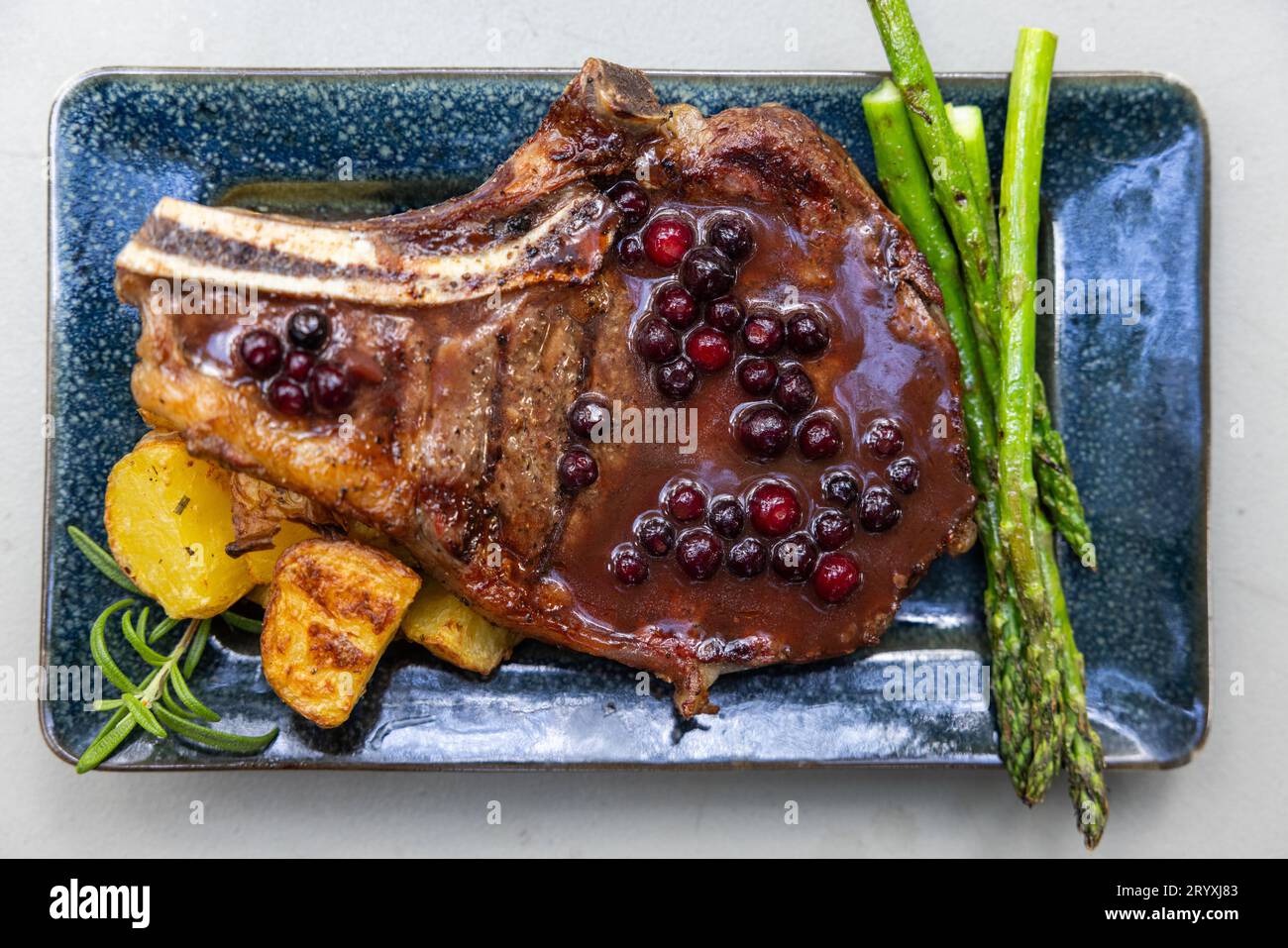 Gegrillter Knochen in Ribeye, serviert mit Kartoffeln und Sparragus, belegt mit einer frischen Huckleberry Portreduktion Stockfoto