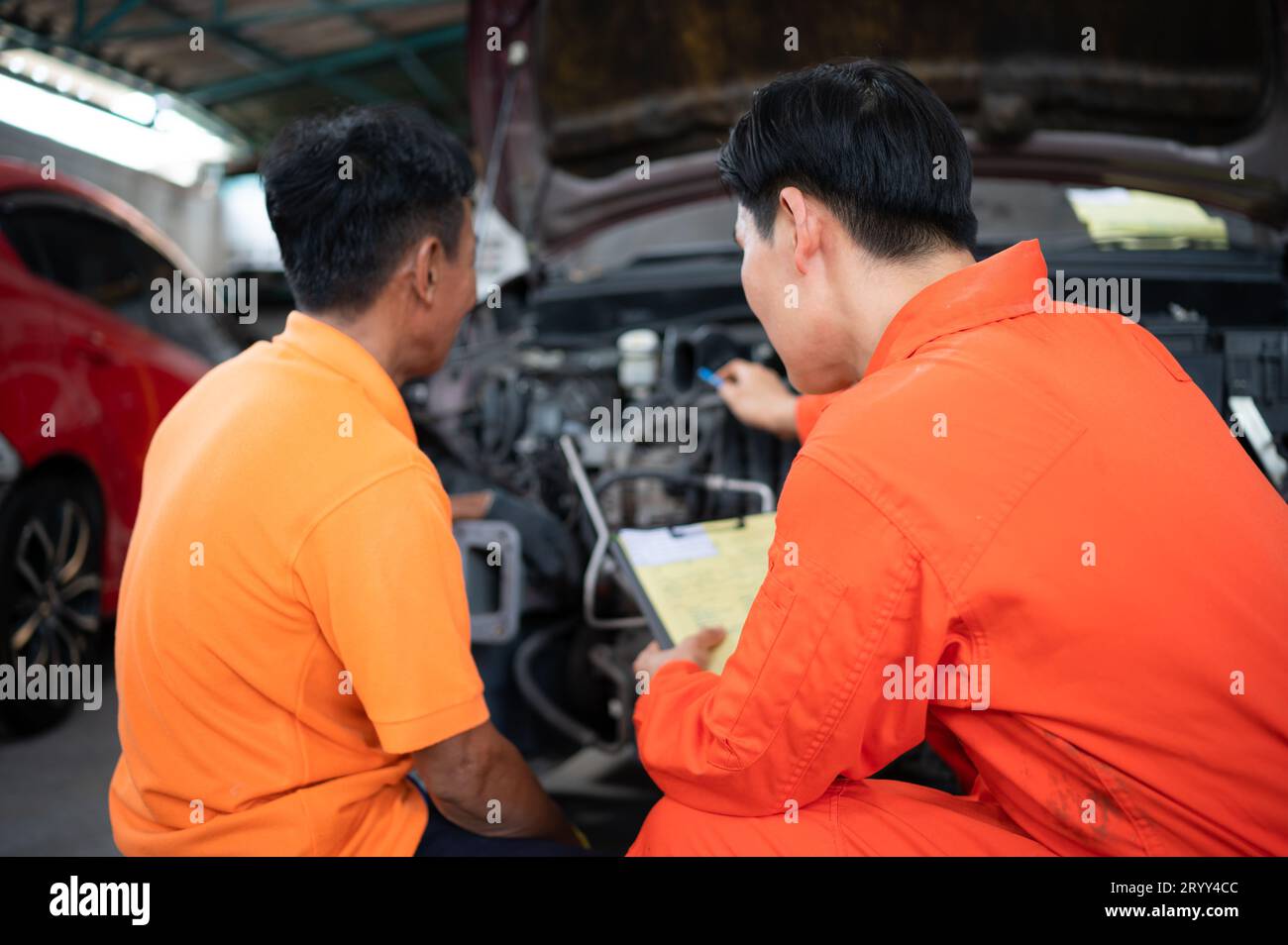 Beide Automechaniker prüfen den Motor eines Kundenfahrzeugs, das zur Reparatur in einer Werkstatt gebracht wird. Stockfoto