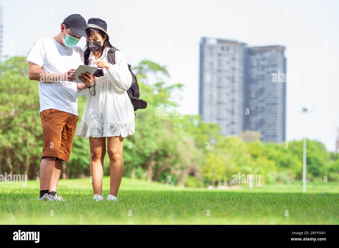 Asiatische Paare mit Gesichtsmaske auf der Suche nach touristischen Informationen durch Tablets von erstaunlichen Orten in der Stadt mit Buildi Stockfoto