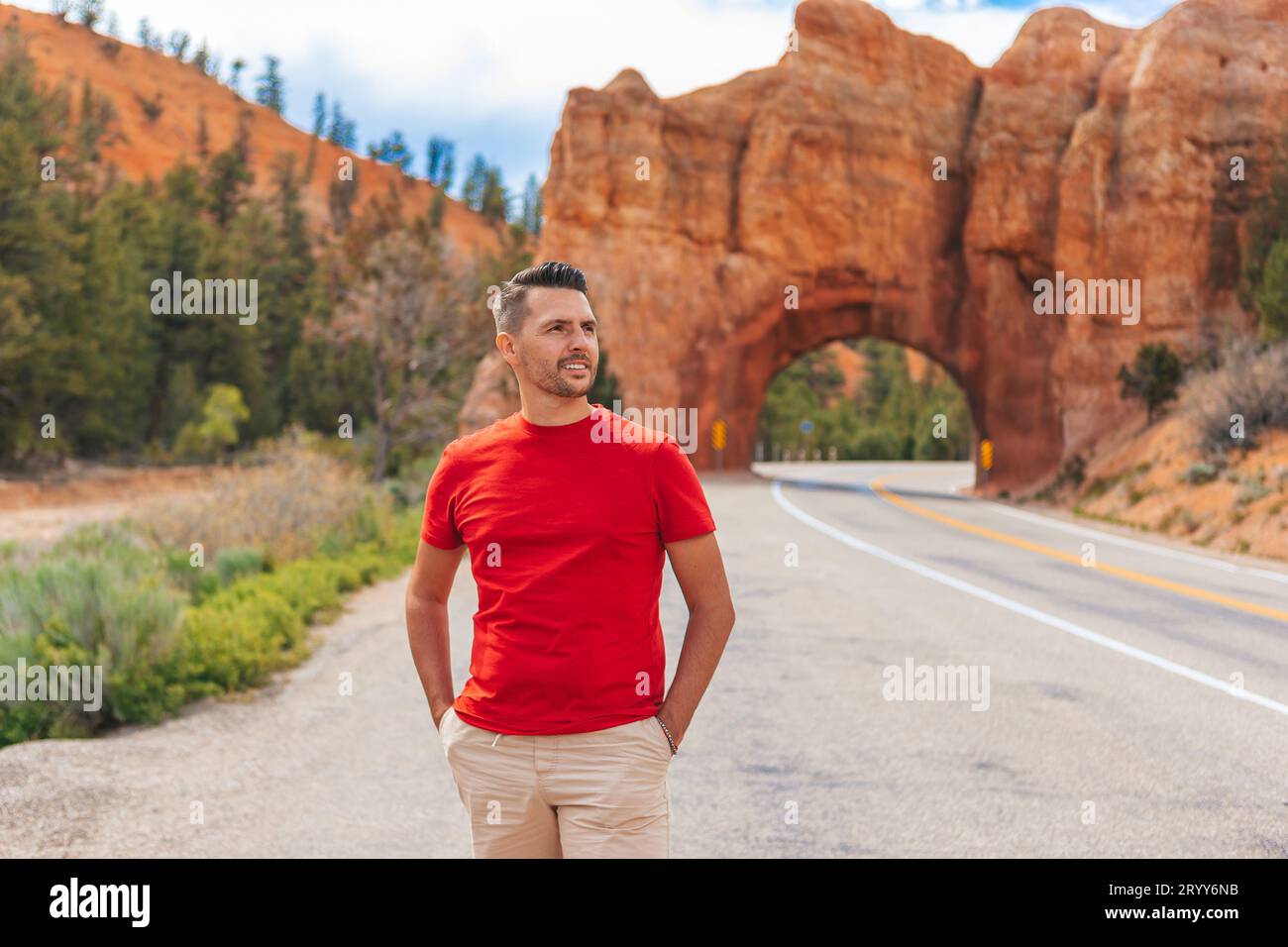 Junger kaukasischer Mann im Hintergrund der Natural Stone Bogenbrücke im Red Canyon National Park in Utah, USA. Natursteinbogen Stockfoto