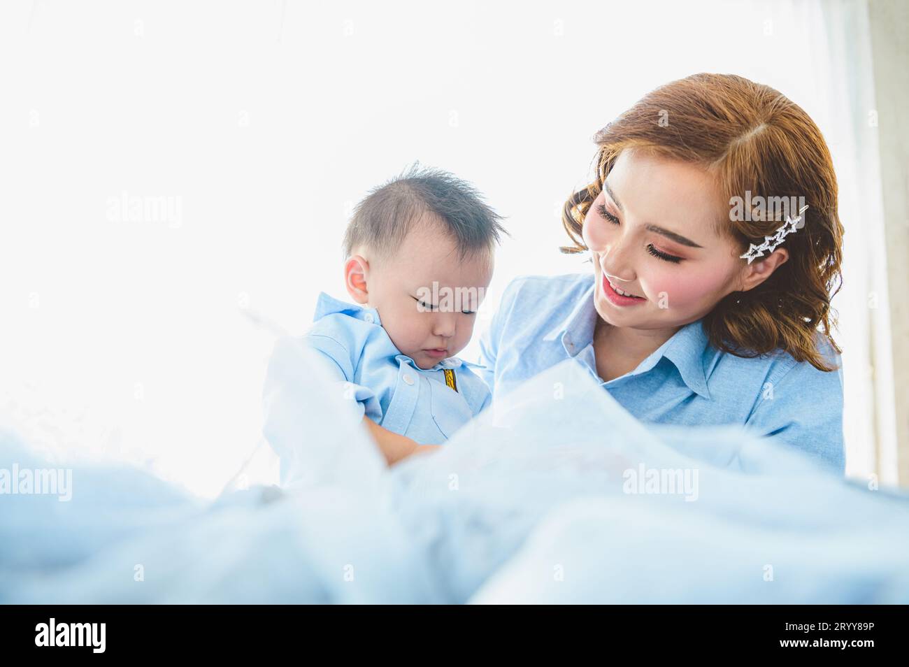 Asiatische Mutter und ihr Sohn tragen blaue Hemden im Schlafzimmer mit Kopierraum zu Hause. Menschen Lebensstil und Neugeborene medizinische Betrüger Stockfoto