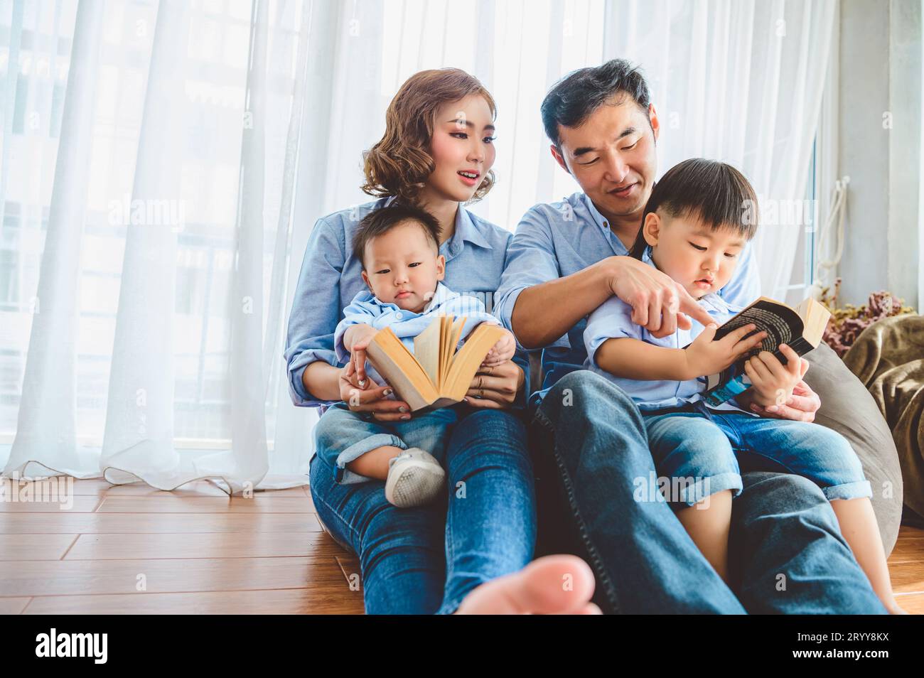 Zwei Eltern bringen ihren Söhnen das Lesen im Wohnzimmer bei. Lernkonzept für Mensch Lifestyle und Bildung. Bundesstaat Quara Stockfoto