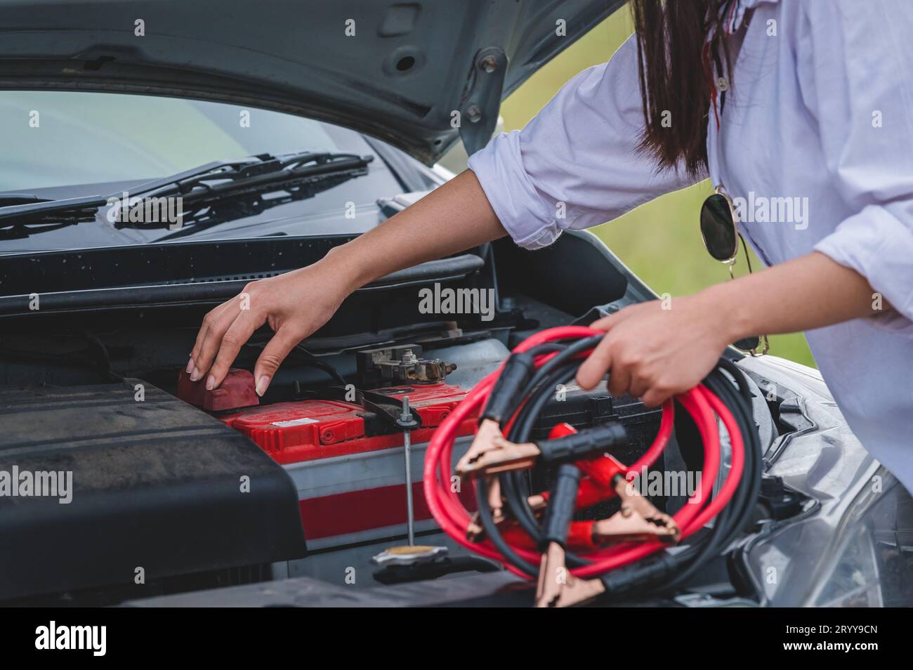 Großaufnahme einer Frau, die das Batteriekabel hält, Kupferdraht für die Reparatur eines defekten Fahrzeugs hält, indem die Batterie mit der roten und schwarzen Linie an e angeschlossen wird Stockfoto