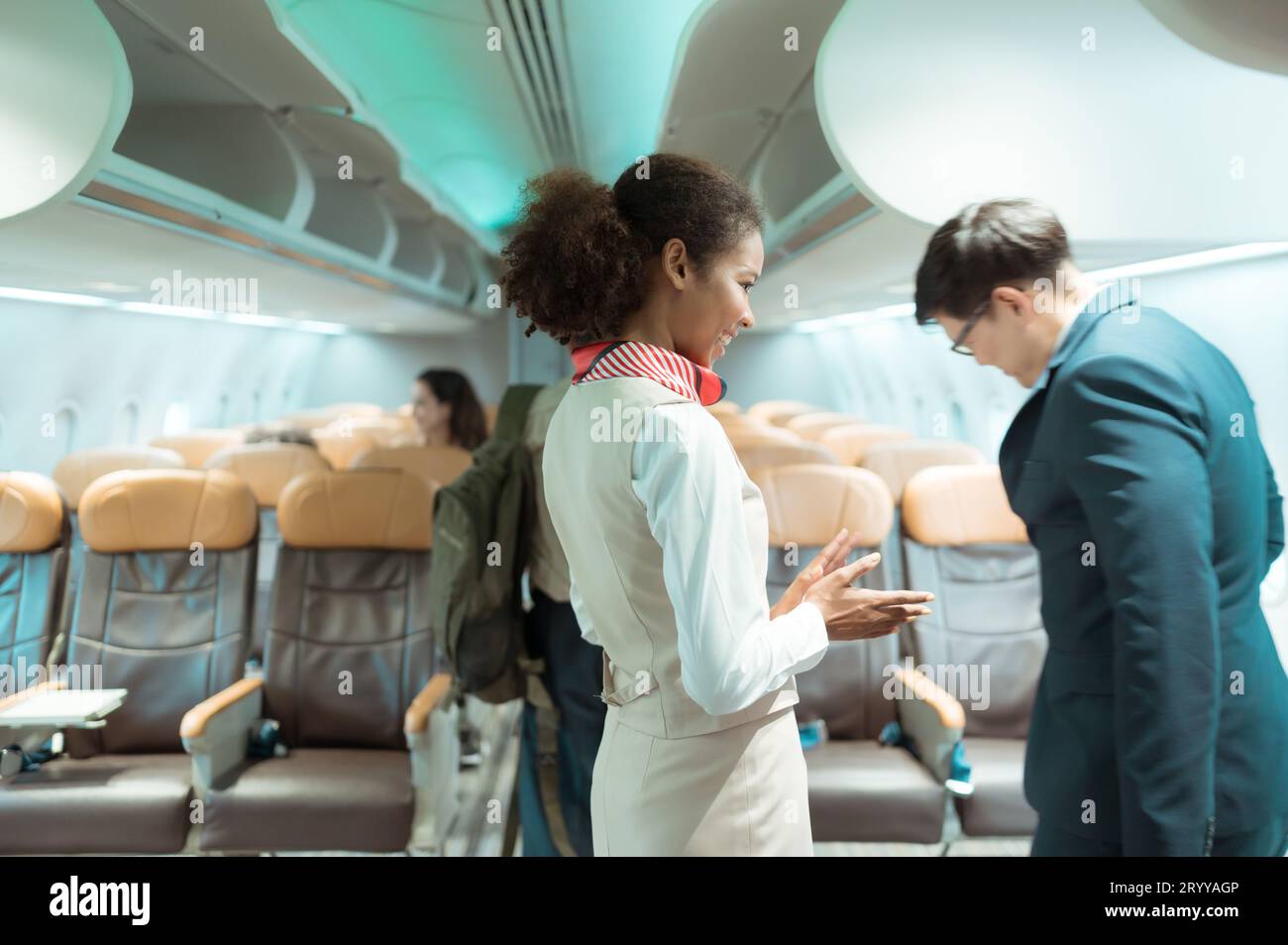 Die Flugbegleiterin begrüßt Passagiere beim Betreten des Flugzeugs, um einen Sitzplatz in der Kabine zu finden. Stockfoto