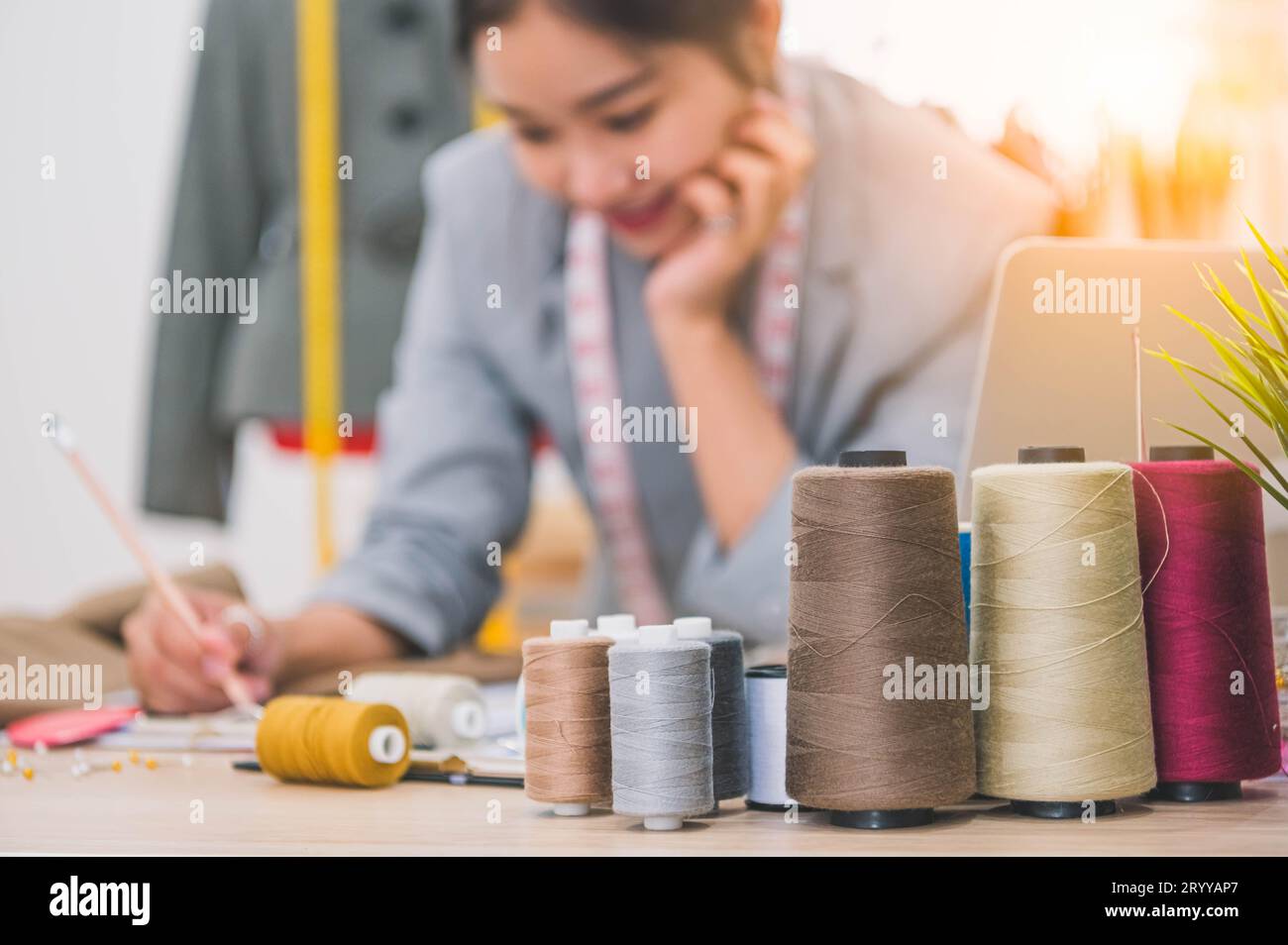 Nahaufnahme des farbigen Fadens mit verschwommenem glücklichen weiblichen Schneider und Nähen Kleidung Stylist Designer Hintergrund. Frau, die neue Coll erstellt Stockfoto