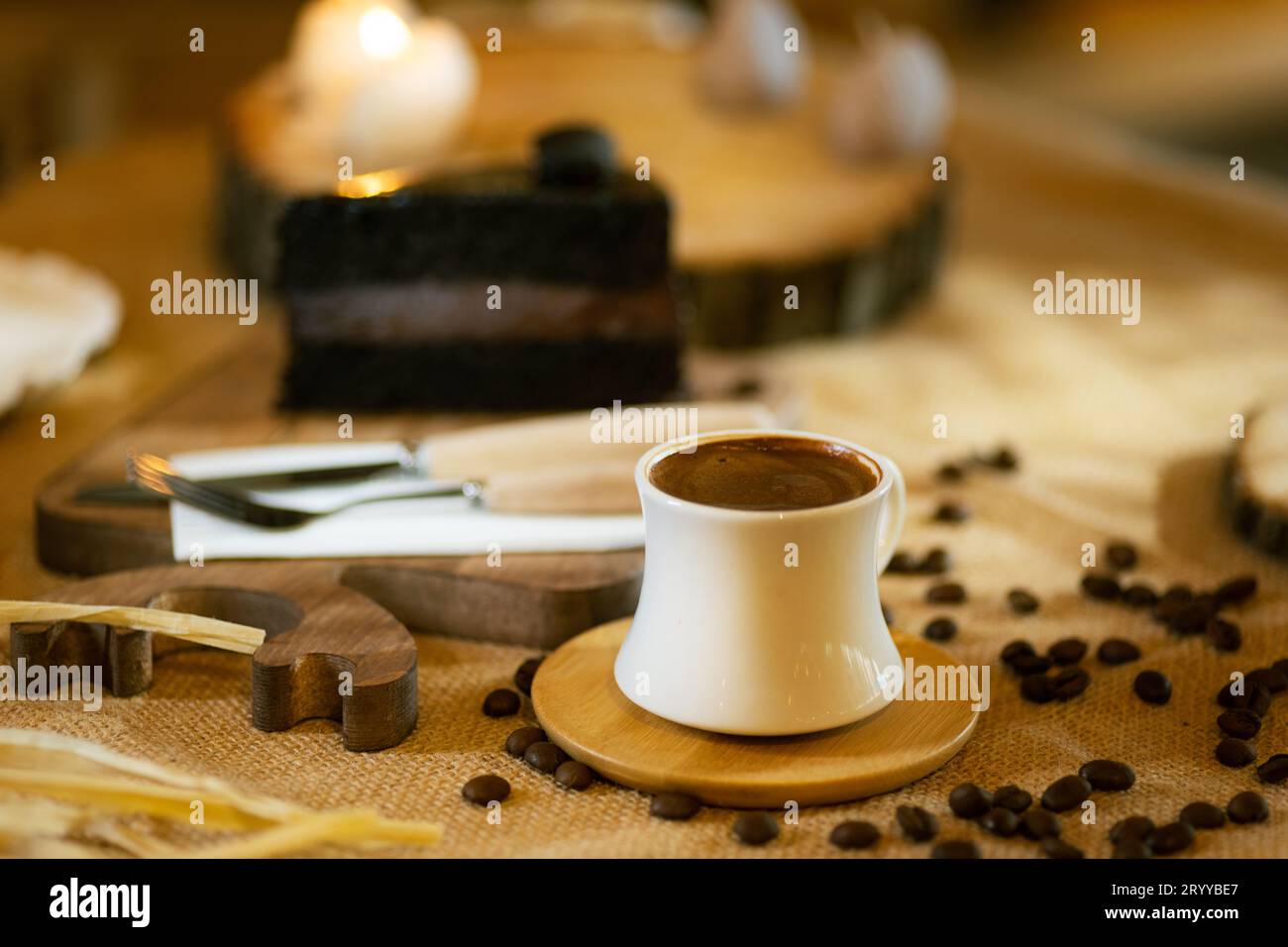 Eine Tasse türkischer Kaffee steht im Mittelpunkt, ergänzt durch ein Stück Schokoladenkuchen, Kaffeebohnen und stimmungsvolle Beleuchtung. Stockfoto