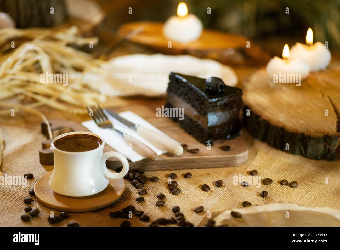 Eine Tasse türkischer Kaffee steht im Mittelpunkt, ergänzt durch ein Stück Schokoladenkuchen, Kaffeebohnen und stimmungsvolle Beleuchtung. Stockfoto