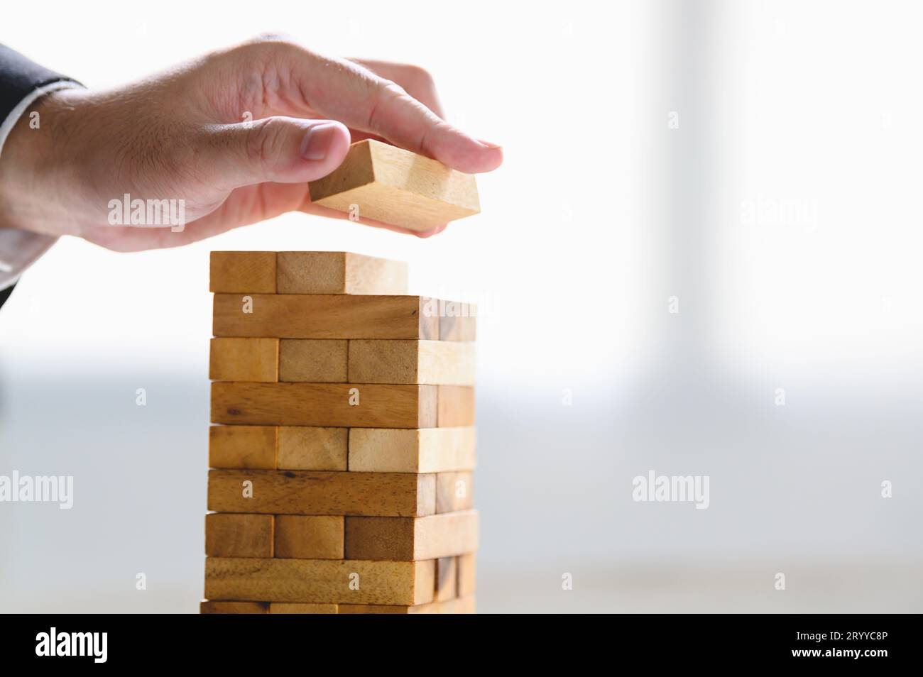 Geschäftsmann arrangiert Holzblock und stapelt als Turm von Hand. Fortschritte bei der Unternehmensorganisation und dem Wachstum des Unternehmens. Erfolg von St Stockfoto