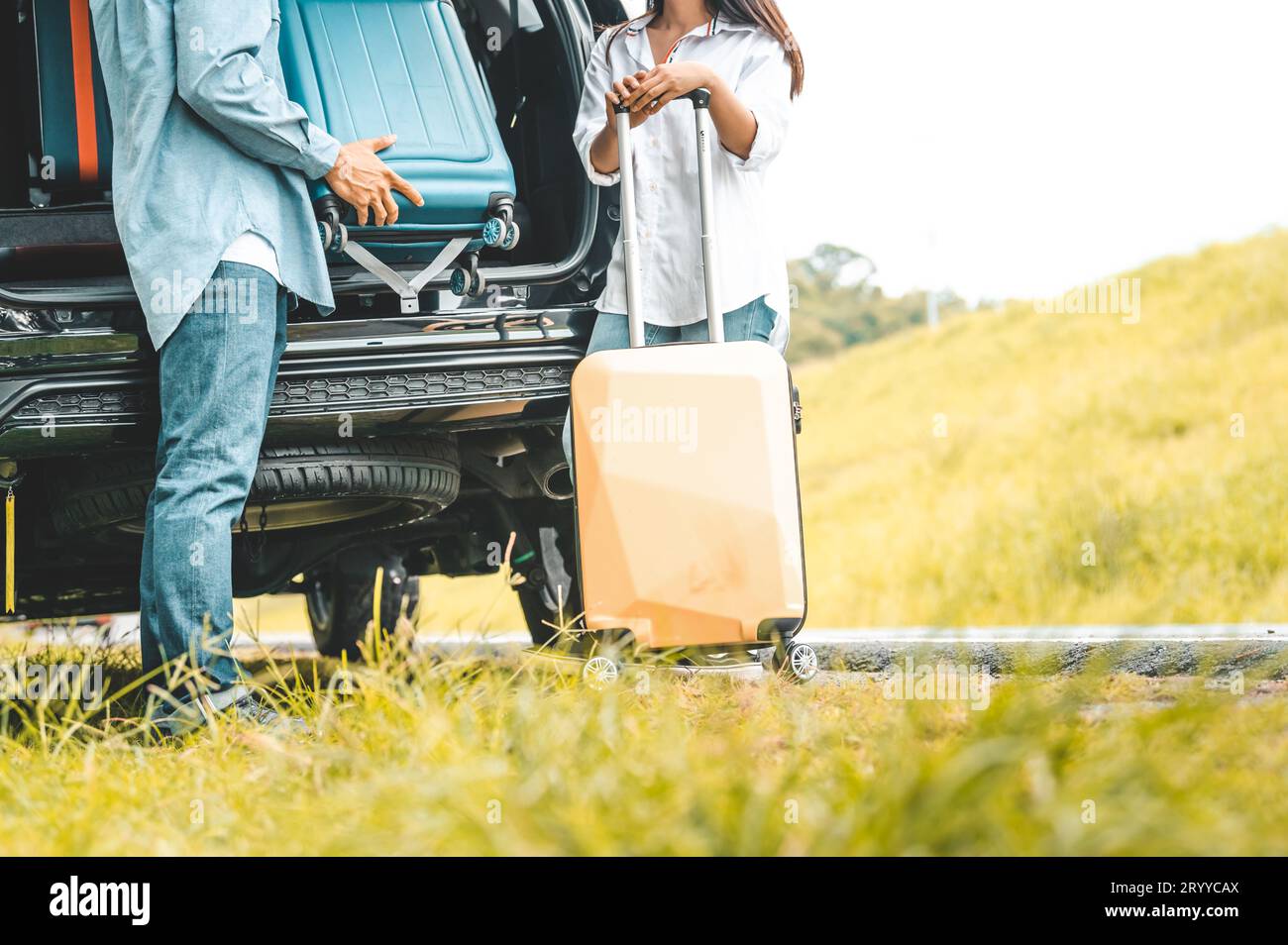 Nahaufnahme unterer Körper des Paares Heben Sie das Trolley-Gepäck auf der Rückseite des SUV-Kofferraums auf einem Roadtrip mit herbstlichem Bergberg-Backgro herunter Stockfoto