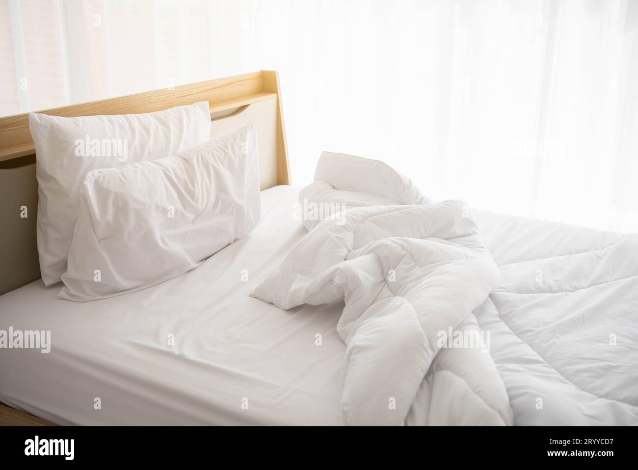 Weißes, ungebautes Bett am Morgen mit Sonnenschein mit weißem Vorhanghintergrund in elegantem Haus. Inneneinrichtung und luxuriöse Möbel Stockfoto