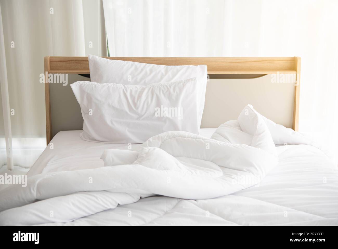 Weißes, ungebautes Bett am Morgen mit Sonnenschein mit weißem Vorhanghintergrund in elegantem Haus. Inneneinrichtung und luxuriöse Möbel Stockfoto