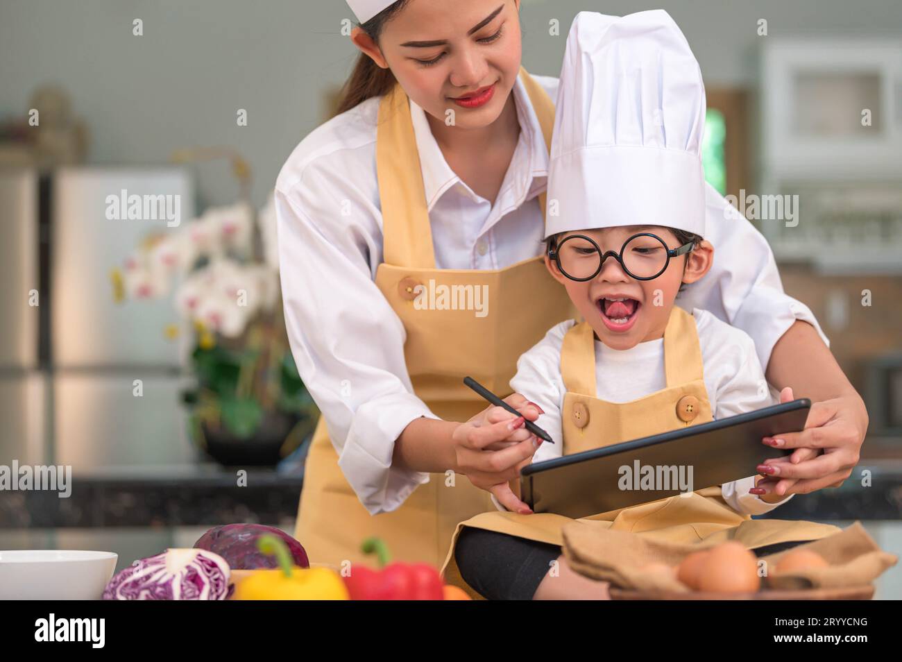 Schöne asiatische Frau und süßer kleiner Junge bereiten Online-Shopping und Auflistung von Zutaten für das Kochen in der Küche zu Hause mit Tab Stockfoto