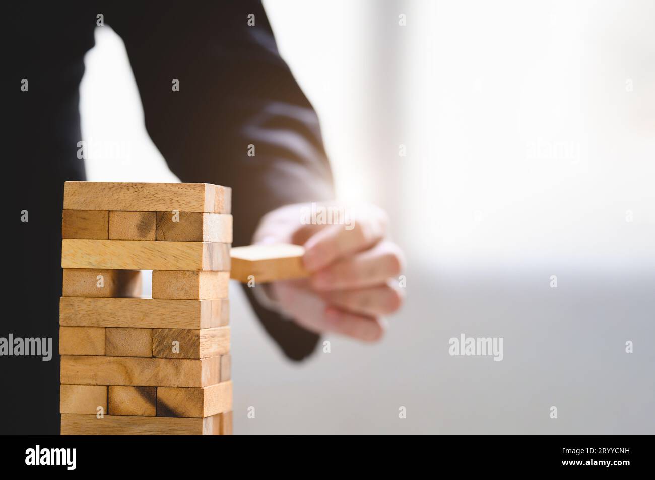 Ein Geschäftsmann nimmt einen Holzblock auf einem gestapelten Turm von Hand als Startup-Projekt. Geschäftsorganisation und Unternehmenswachstum Stockfoto