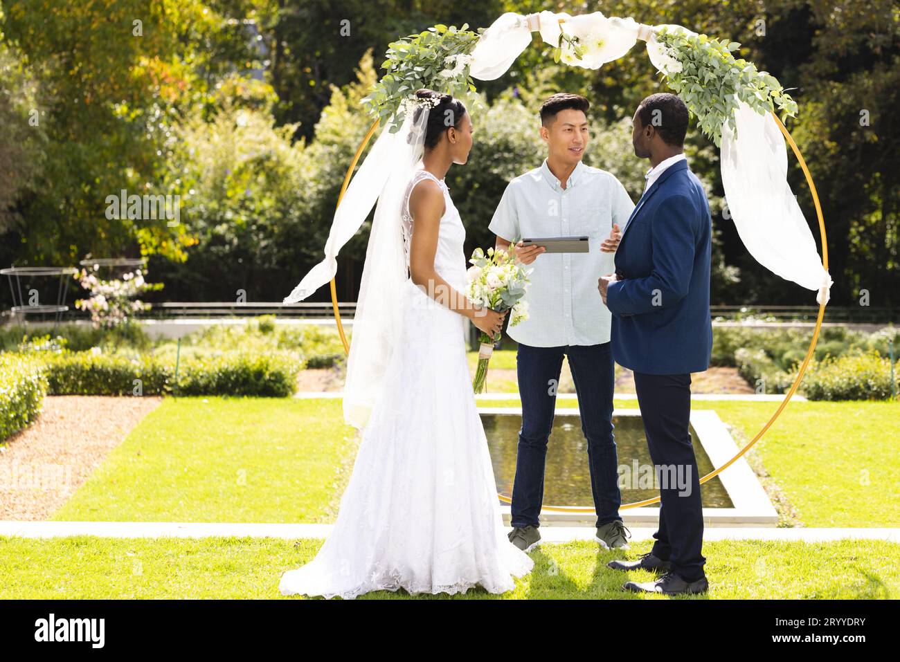 Fröhlicher, vielseitiger Beamter, Braut und Bräutigam bei einer Hochzeit im Freien im sonnigen Garten, Kopierbereich Stockfoto