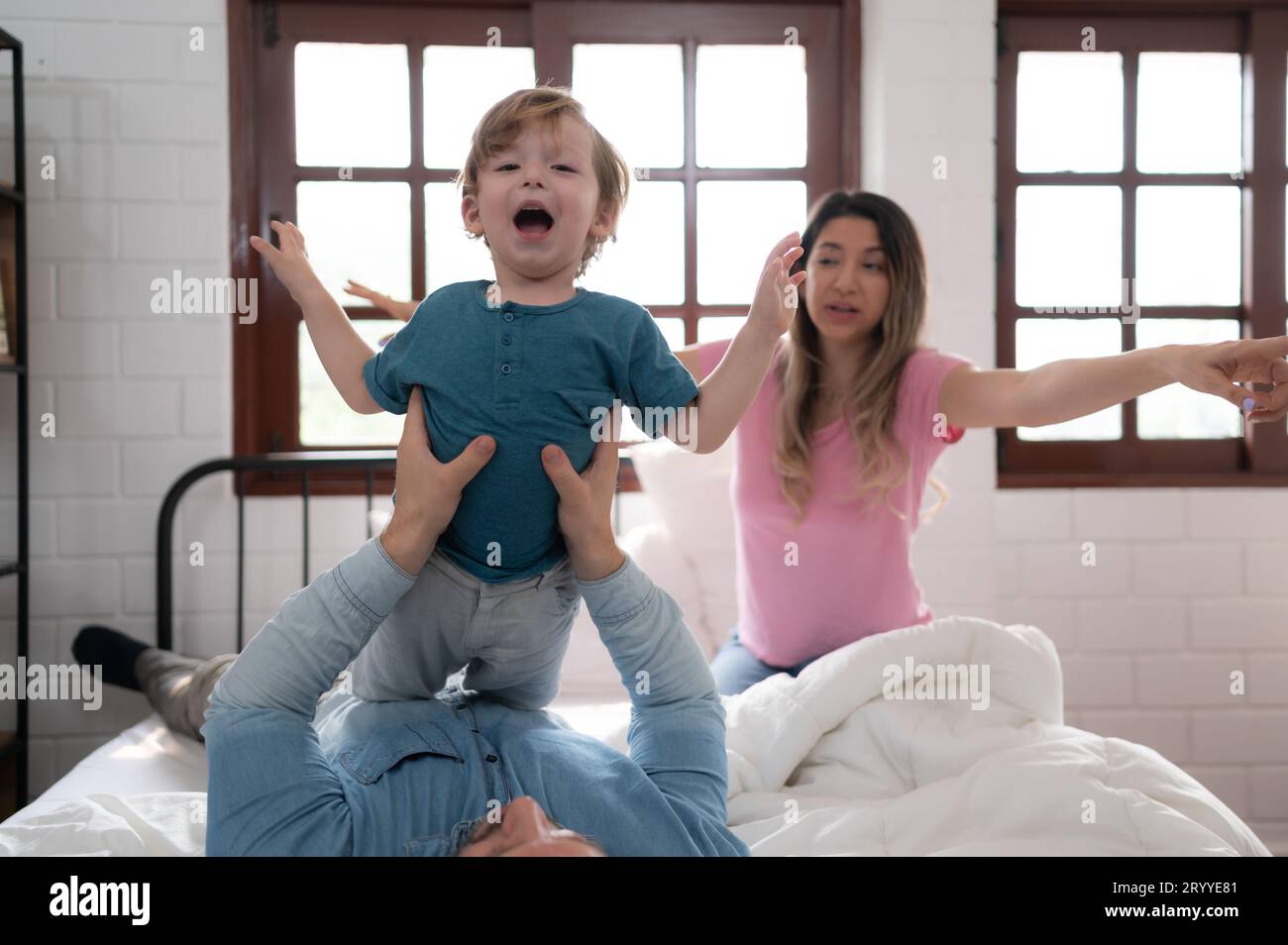 Kleiner Junge, der mit Vater flog, benutzte seine Beine, um ihm zu helfen, hoch vom Boden seines Bettes im Schlafzimmer zu fliegen. Stockfoto