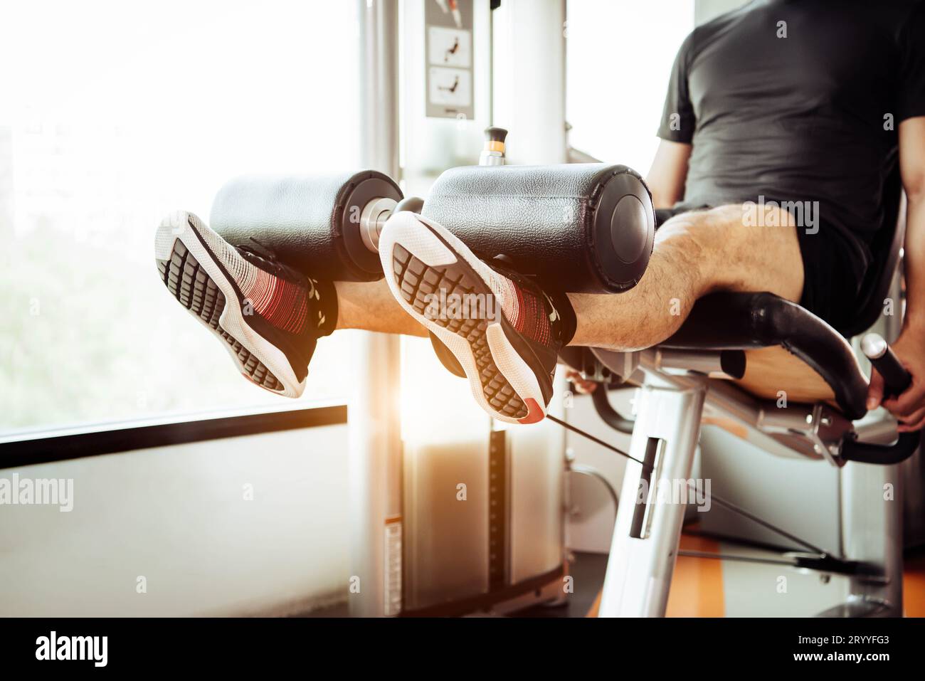 Nahaufnahme eines Mannes, der das Gewicht mit zwei Beinen zum Dehnen der Muskeln im Fitness-Studio im privaten Wohnungs-Hintergrund trägt. Sport und PEO Stockfoto