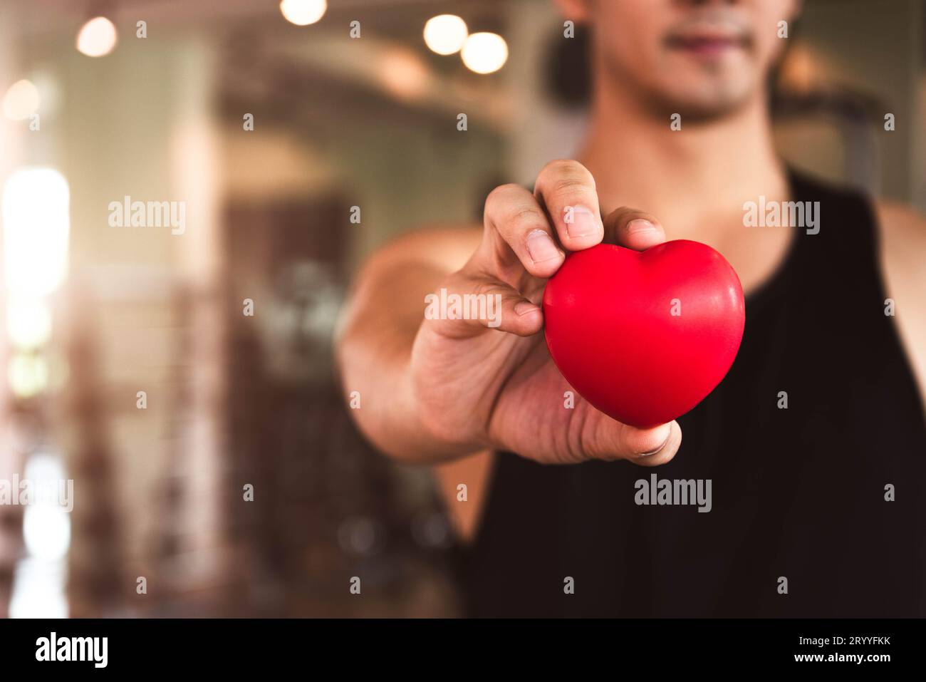 Glücklicher Sportmann, der rotes Herz im Fitness-Fitnessclub hält. Medizinisches Herz-Kreislauf-Krafttraining Lebensstil. Gutaussehender Sport, männlich Stockfoto