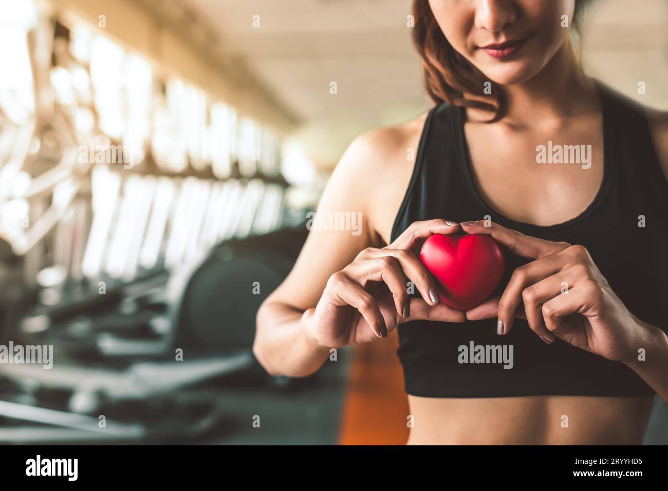 Glückliche Sportfrau mit rotem Herzen im Fitness-Studio-Club. Medizinisches Cadio Herz Krafttraining Lebensstil. Hübscher weiblicher Sport-Gi Stockfoto