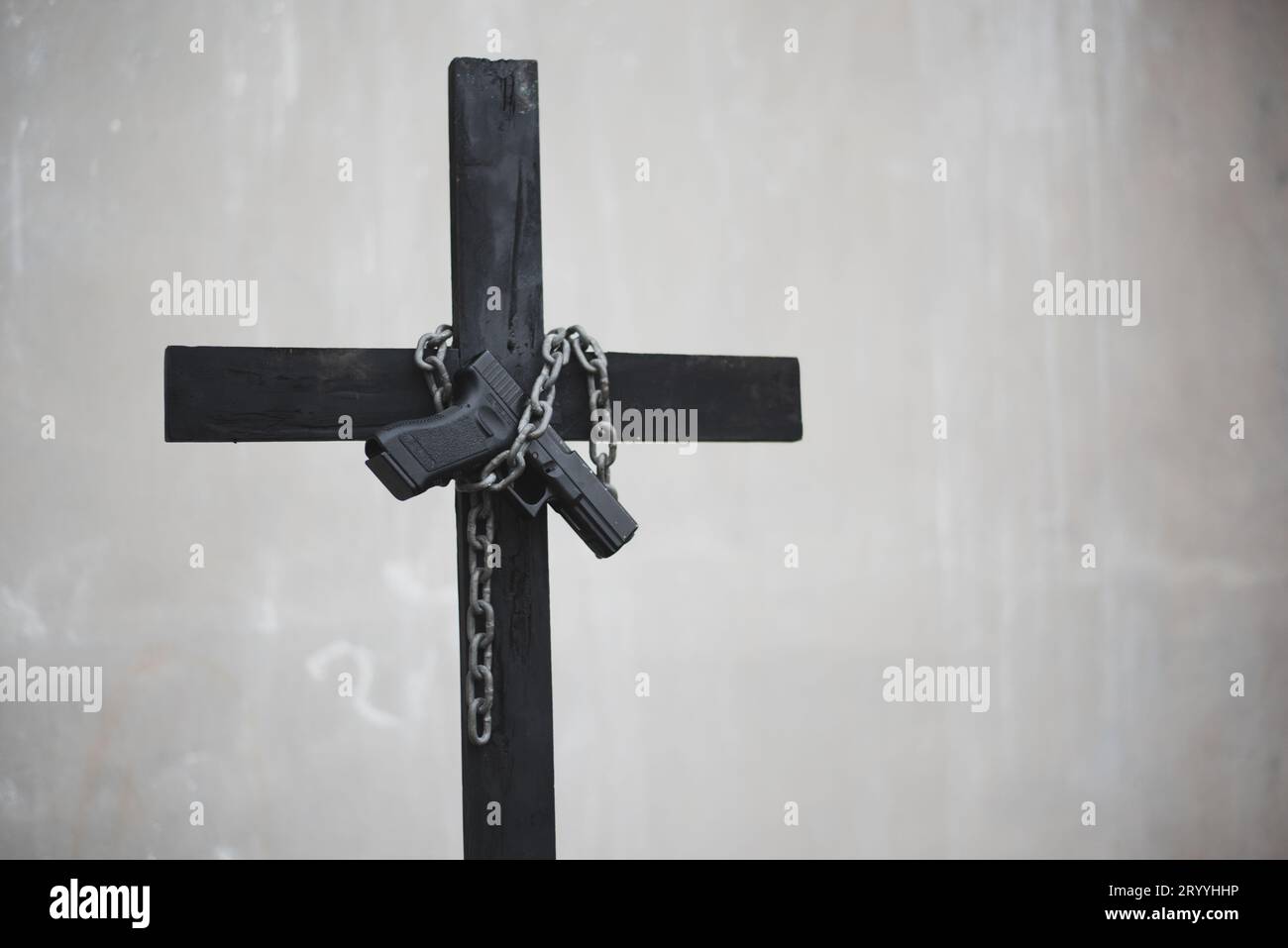 Schwarzes Kreuz mit Kette und Pistole an weißer Grunge-Wand. Objekt- und Waffenkonzept. Thema christliche Religion. Halloween und Crim Stockfoto