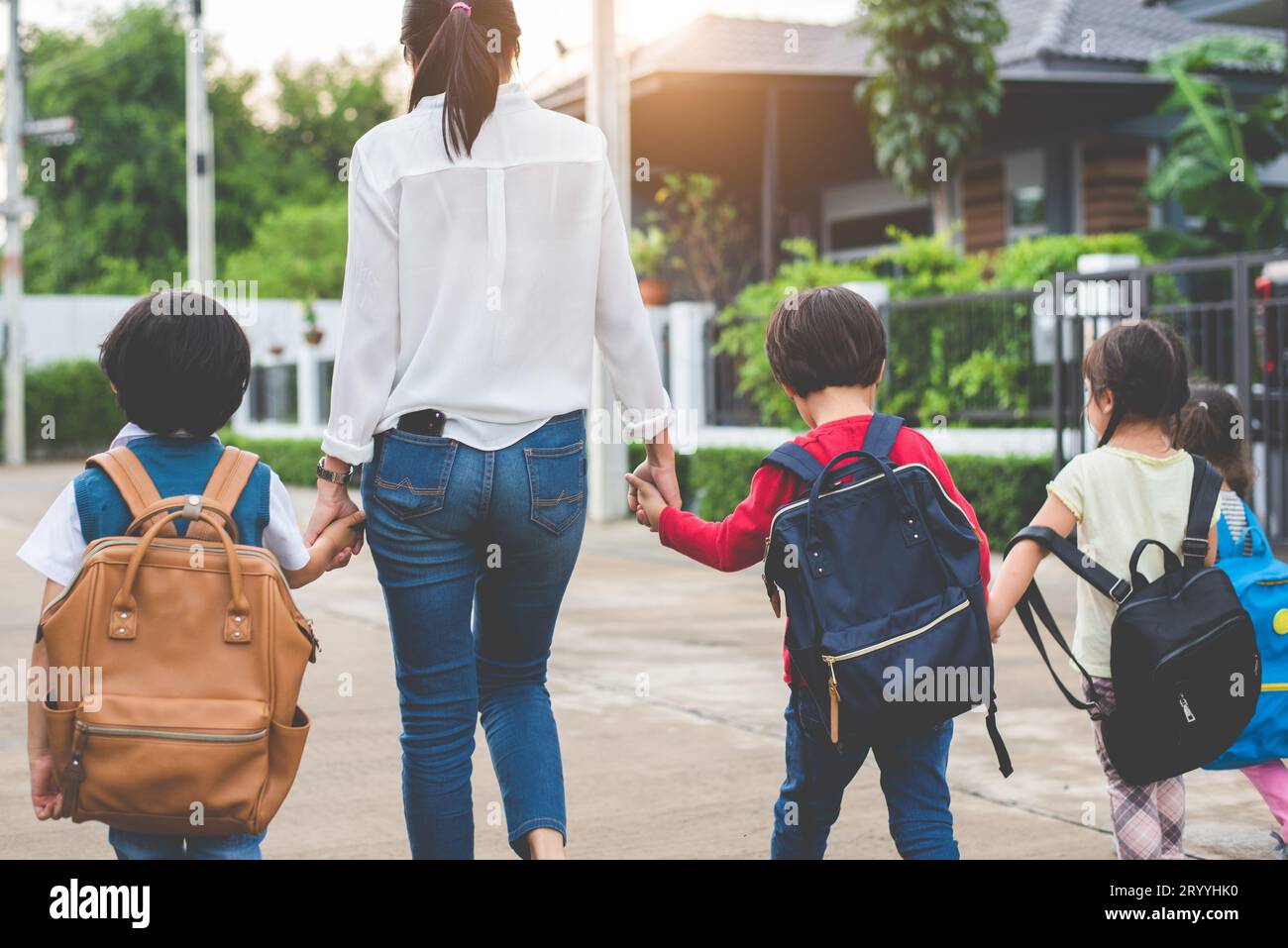 Eine Gruppe von Mutter und Kindern, die Hände halten und mit Schultasche zur Schule gehen. Mom bringt Kinder mit dem Bus zur Schule zusammen mit sa Stockfoto