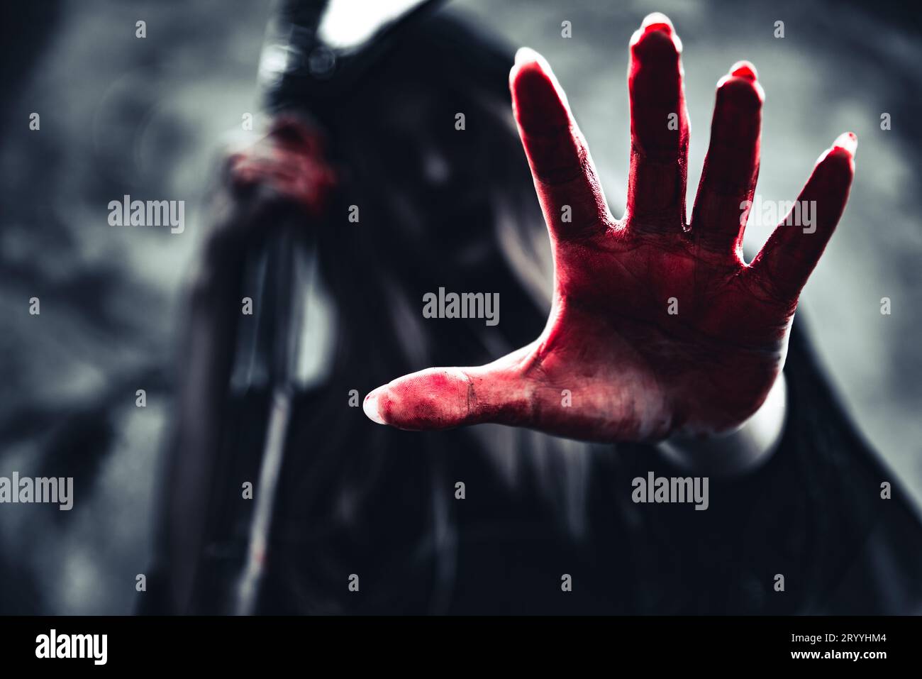 Hexe zeigt blutige Hand mit Sensenmann. Weiblicher Dämonenenengel in schwarzer Kleidung und Kapuze auf Grunge-Wand-Hintergrund. Halloween Tag und Stockfoto